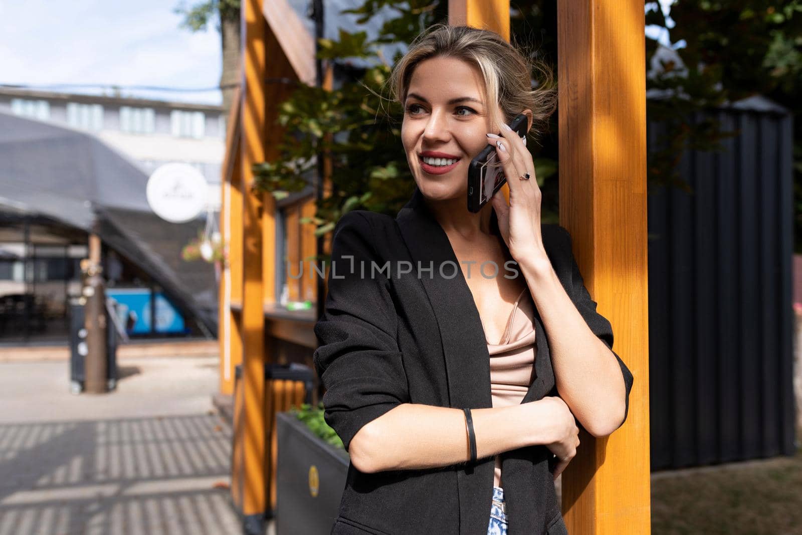 middle-aged woman talking on the phone on the background of the city looks away with a smile on her face.