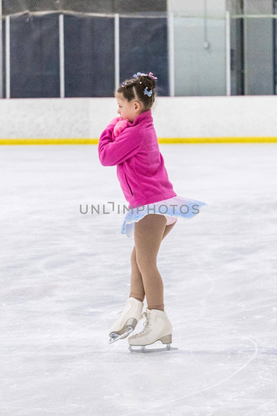 Little girl practicing figure skating on an indoor ice rink.