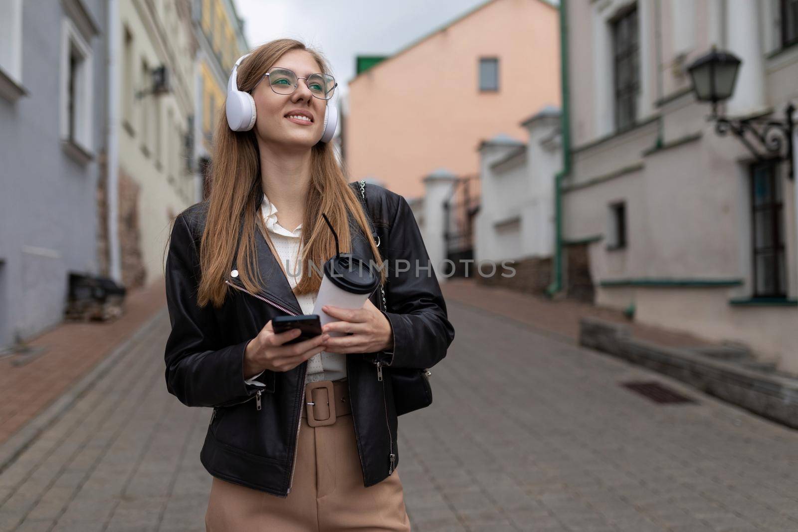 young woman Tourist in headphones with a mobile phone walks through the old city.