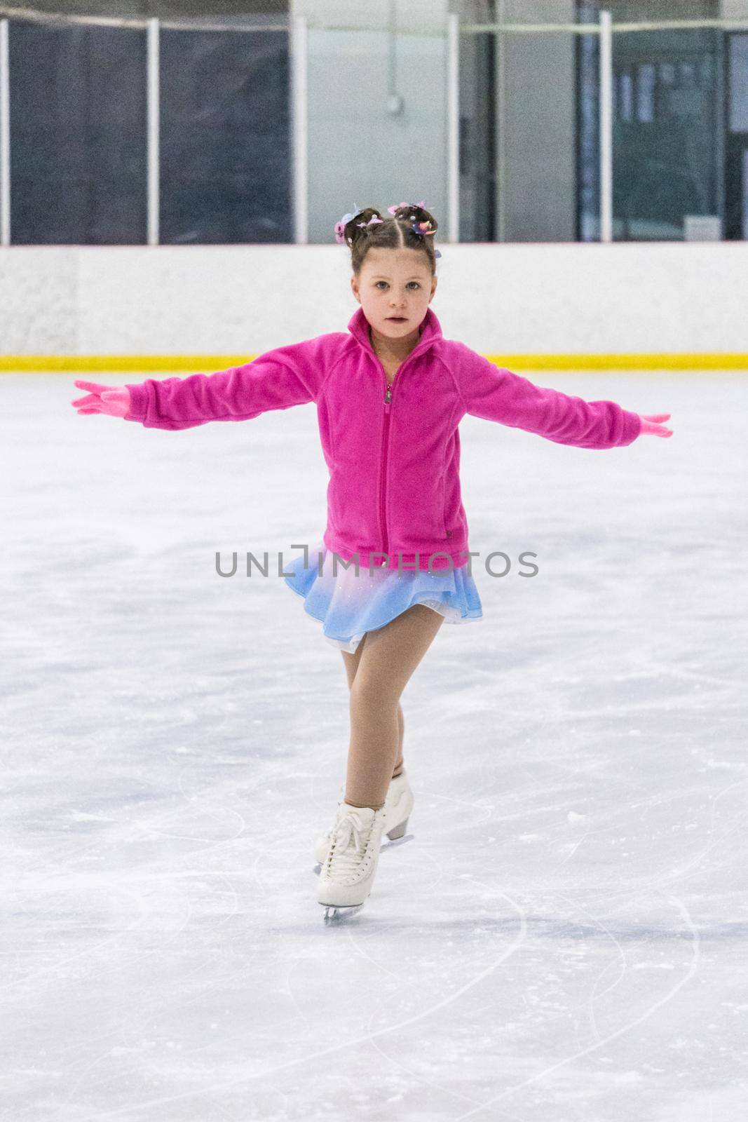 Little girl practicing figure skating on an indoor ice rink.