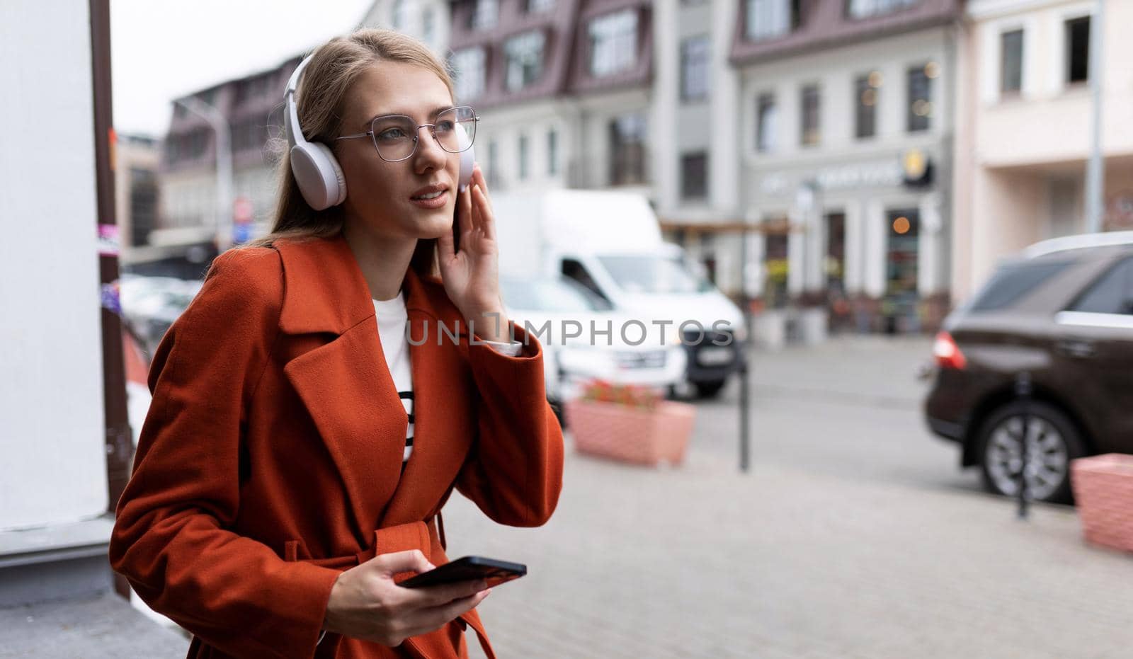 a young woman listens to music in headphones with a phone in her hands against the backdrop of city cafes.