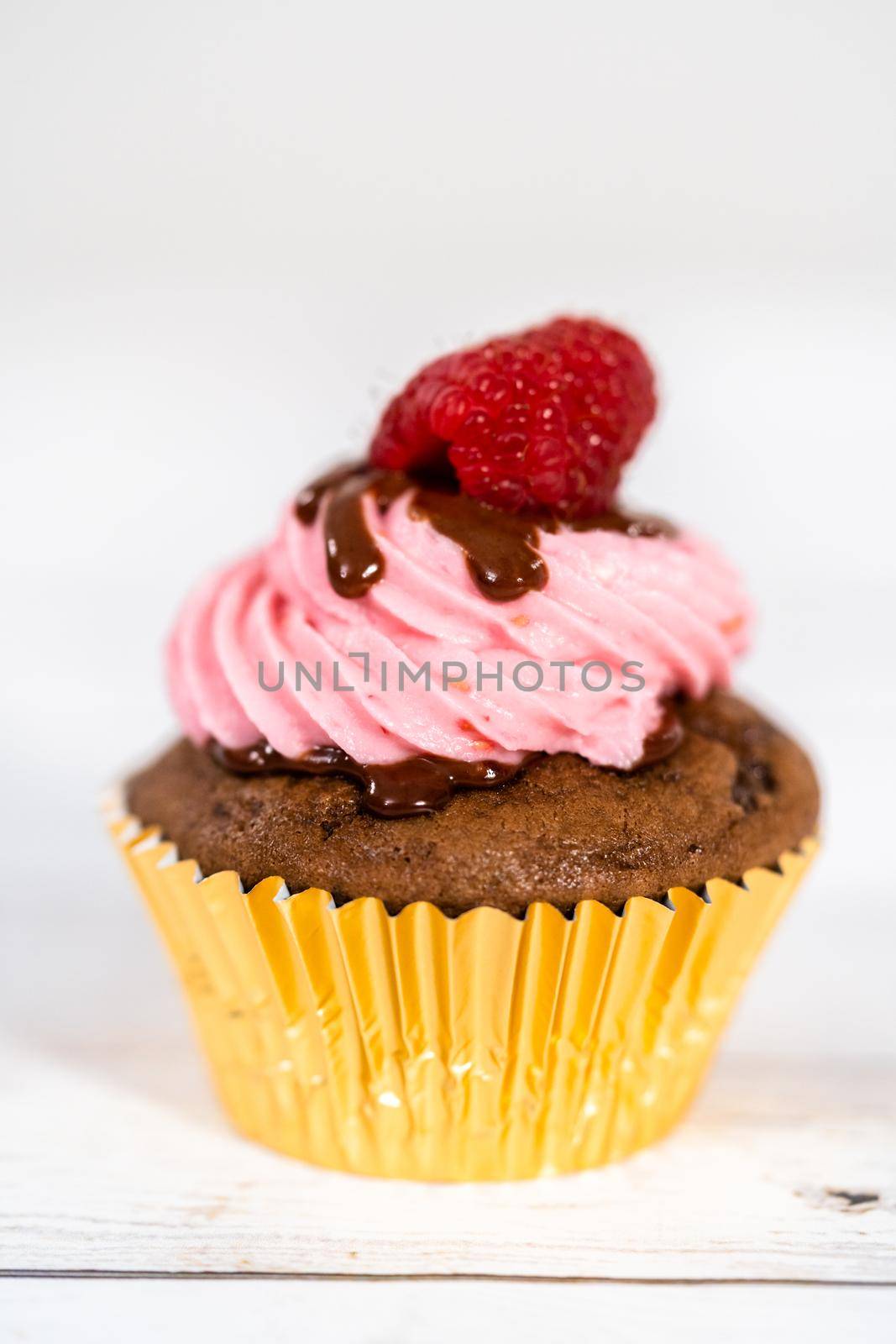 Gourmet chocolate raspberry cupcakes drizzled with chocolate ganache and topped with a fresh raspberry.