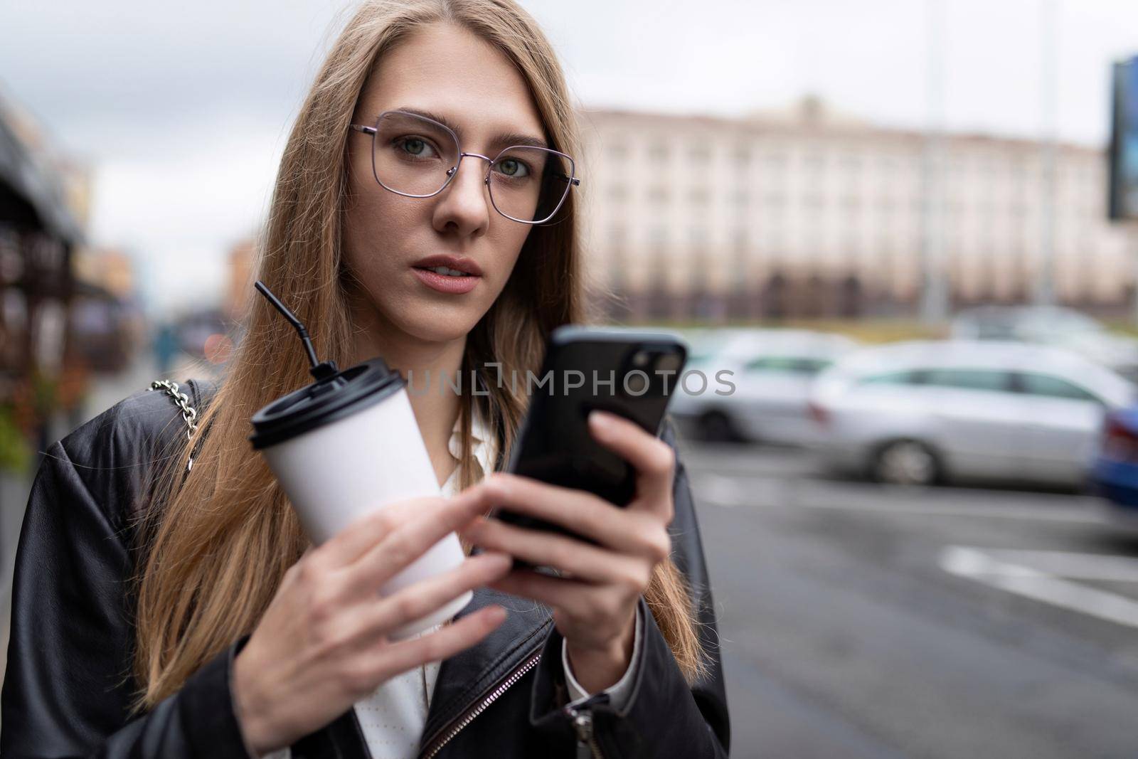 portrait of a serious young woman with a cup of coffee looking at a mobile phone.