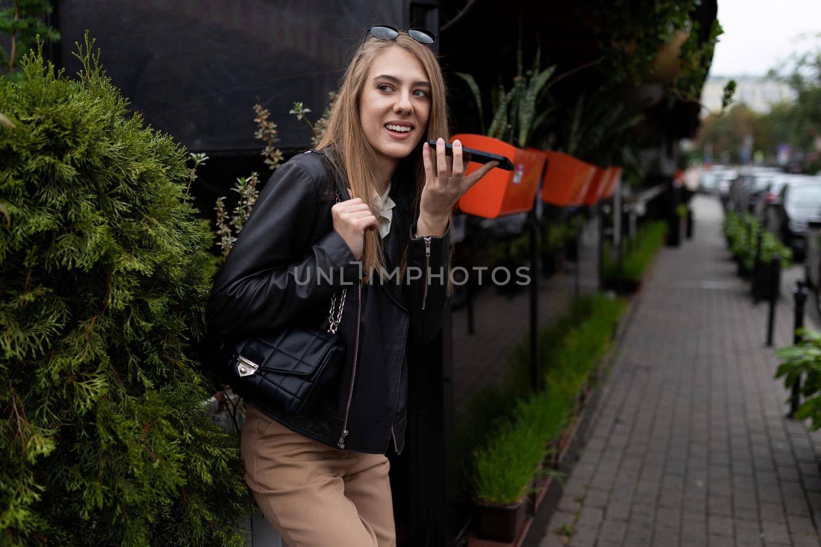 young woman talking on the speakerphone of a mobile phone near a city cafe.
