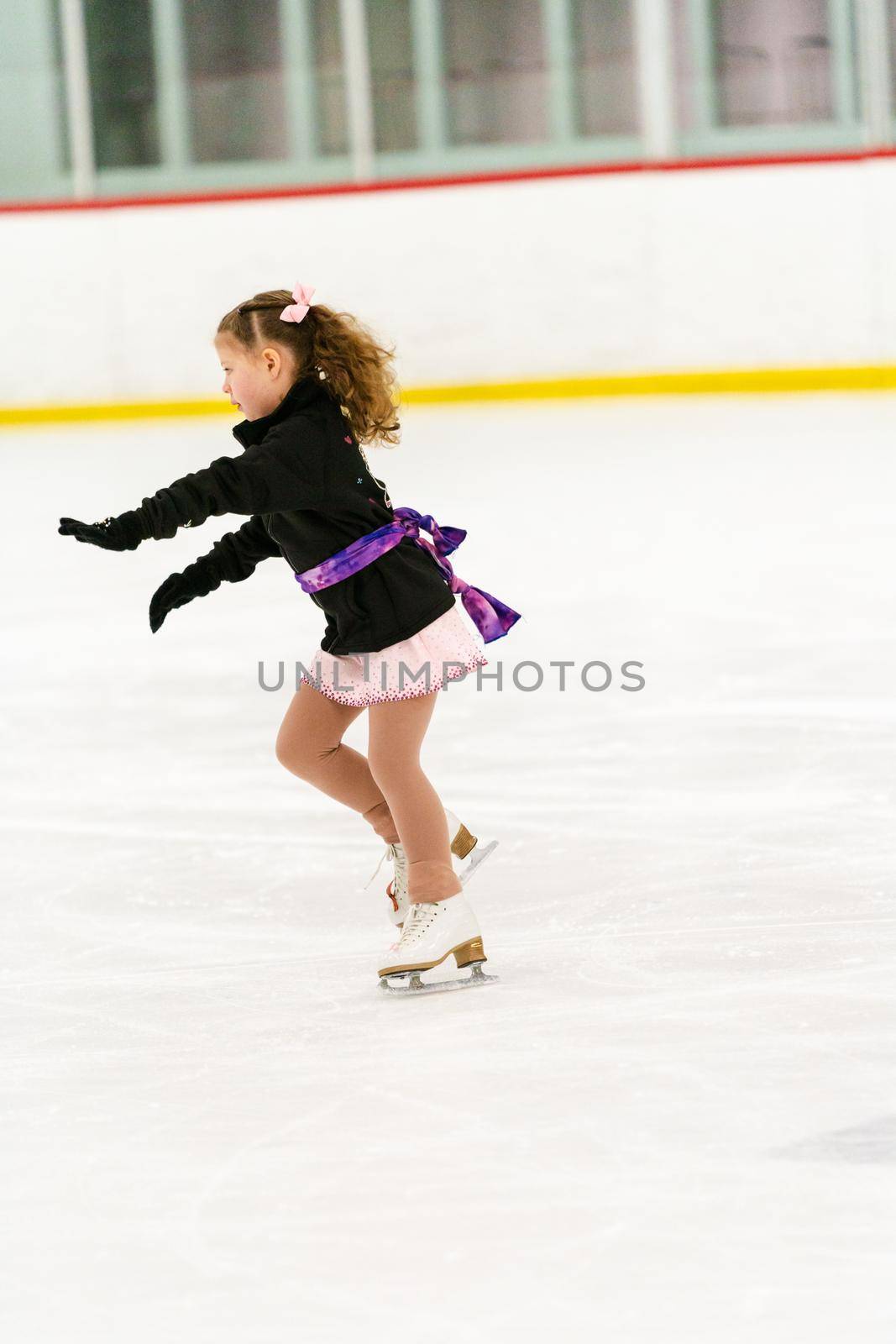 Little girl practicing figure skating on an indoor ice skating rink.