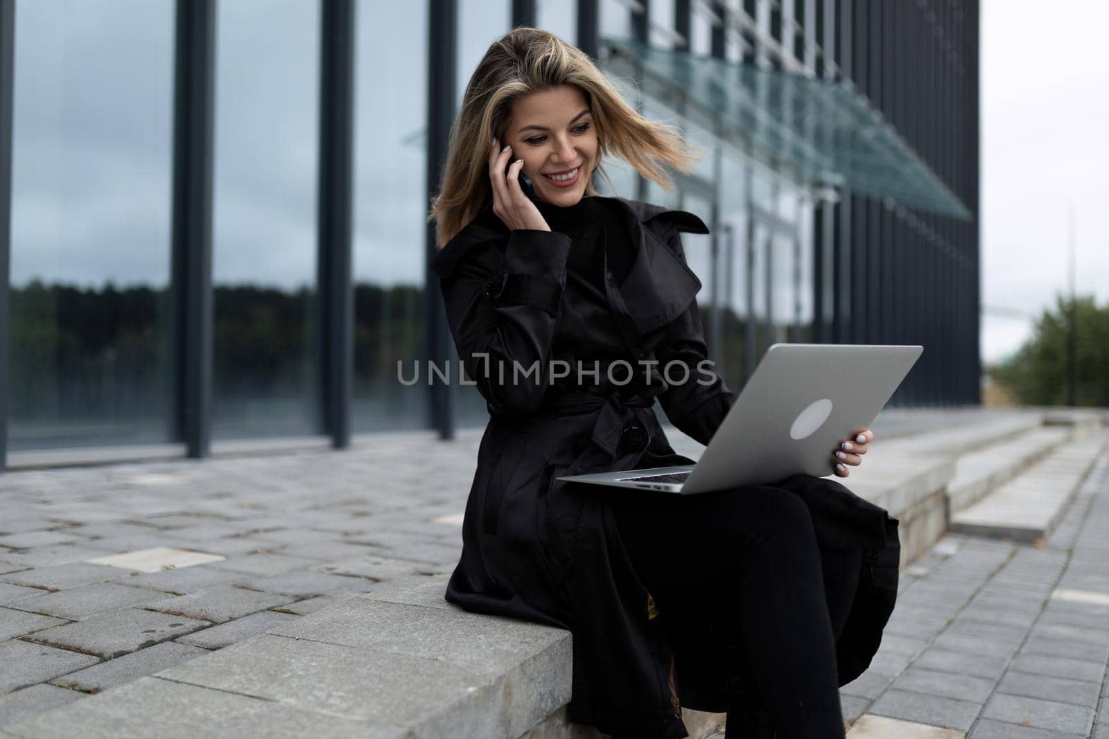 a middle-aged businesswoman woman works online on a laptop against the backdrop of an office building.