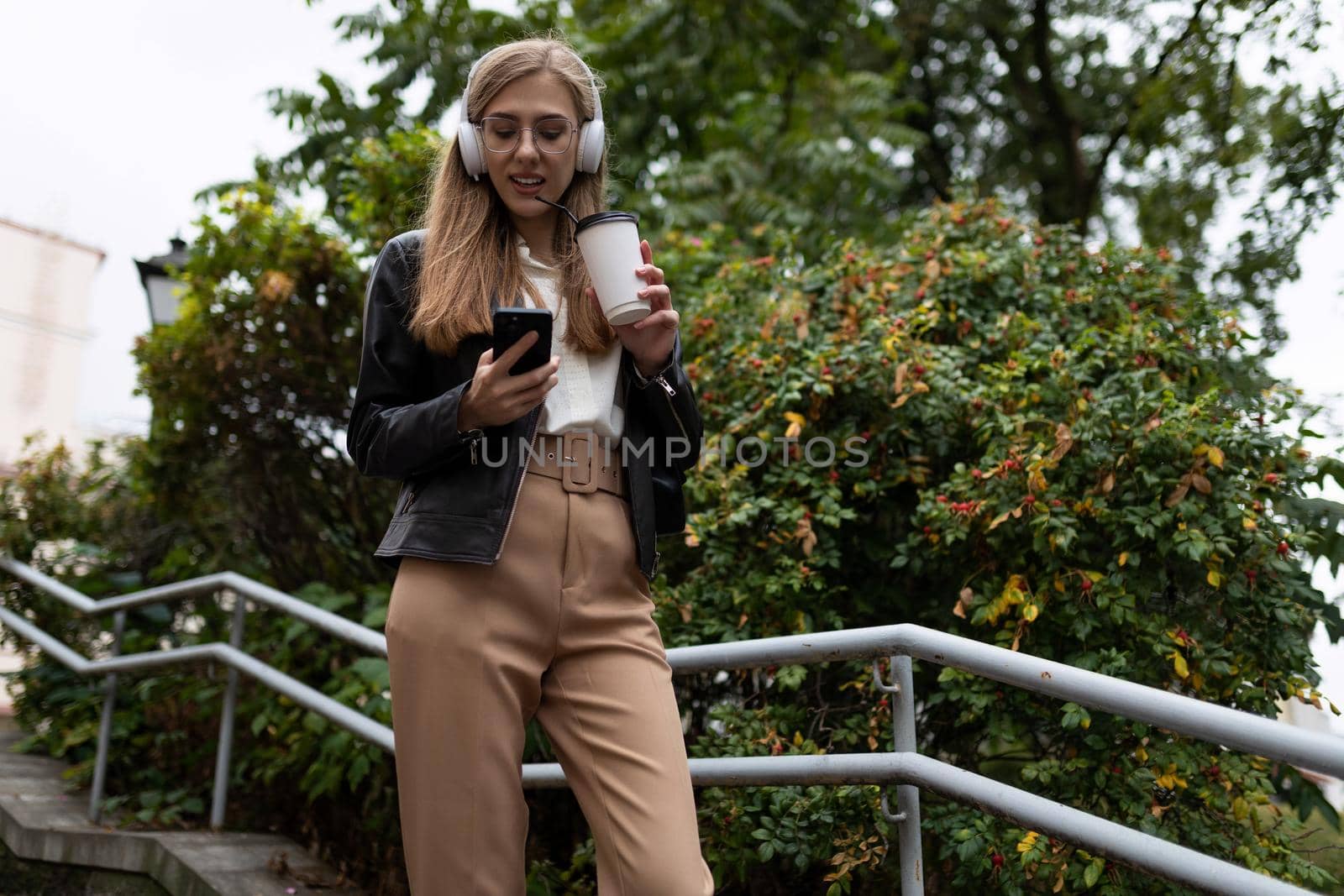 young woman in the city with a glass of coffee in headphones and a mobile phone.