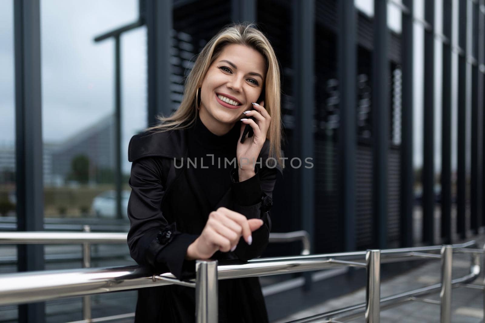 Business woman talking on a mobile phone with a smile looking at the camera on the background of a modern office building.