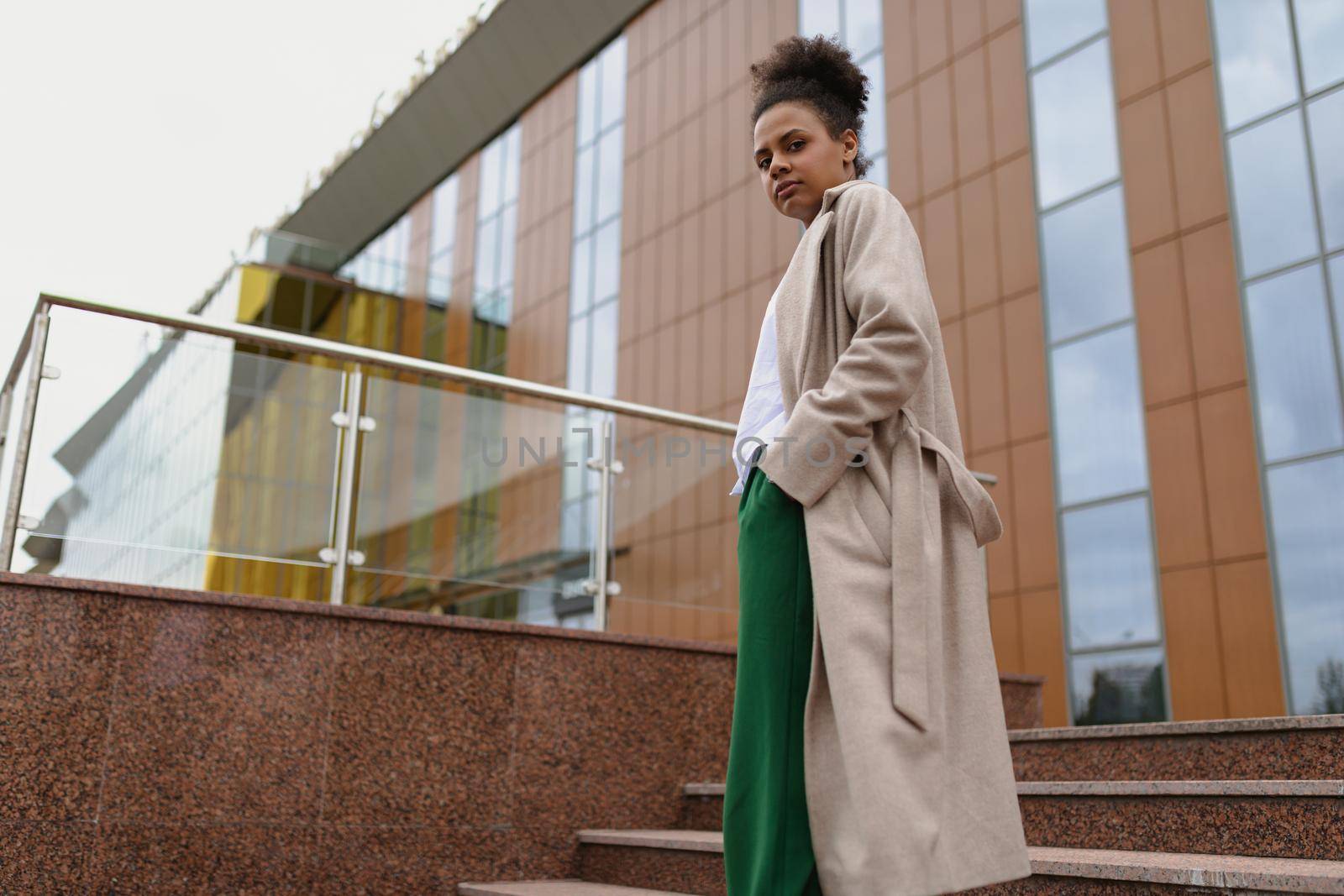confident african american young woman stands in a floor spread against the backdrop of an office building.