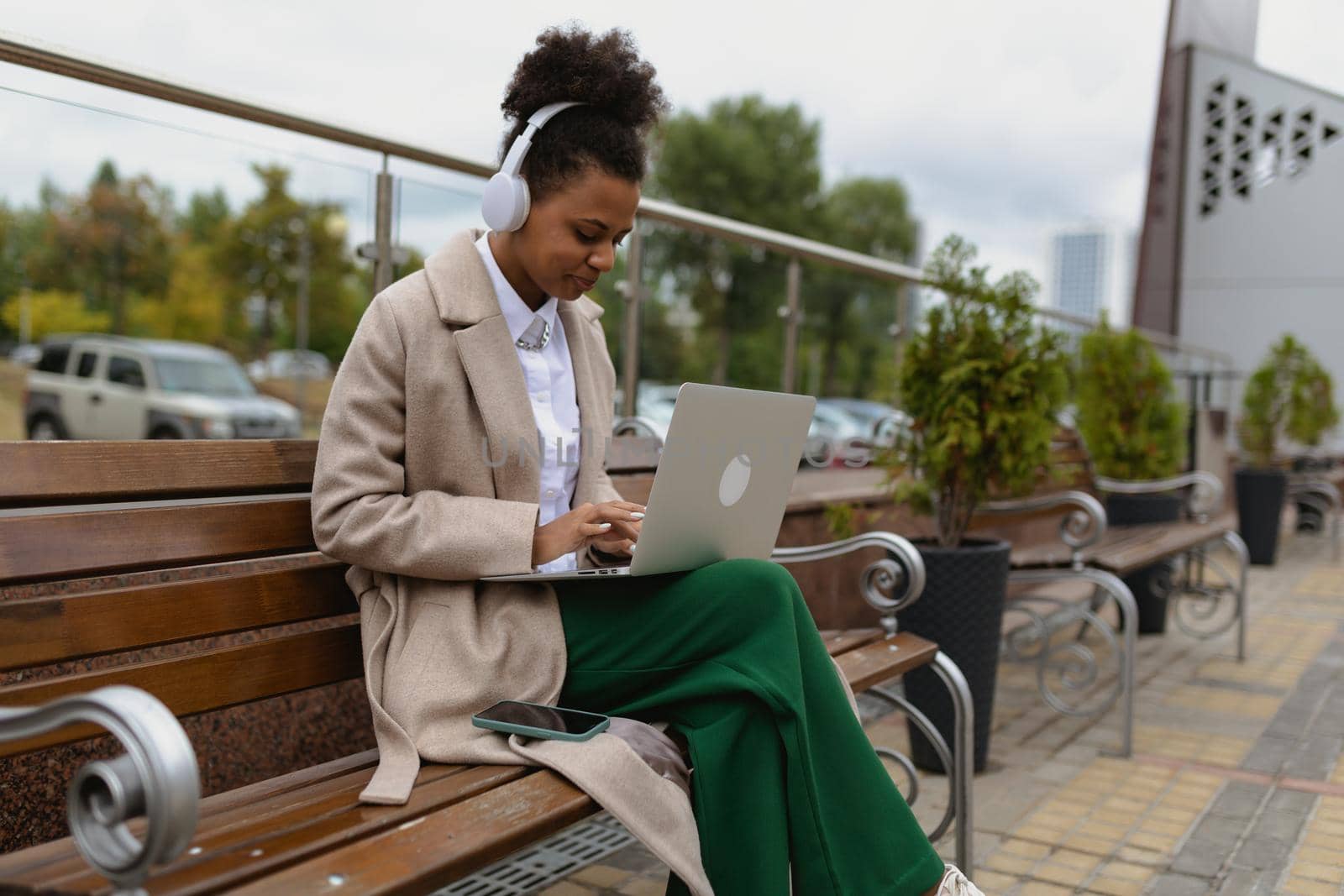 African-American young woman student working online on a laptop with headphones Sitting on a bench near the business center.