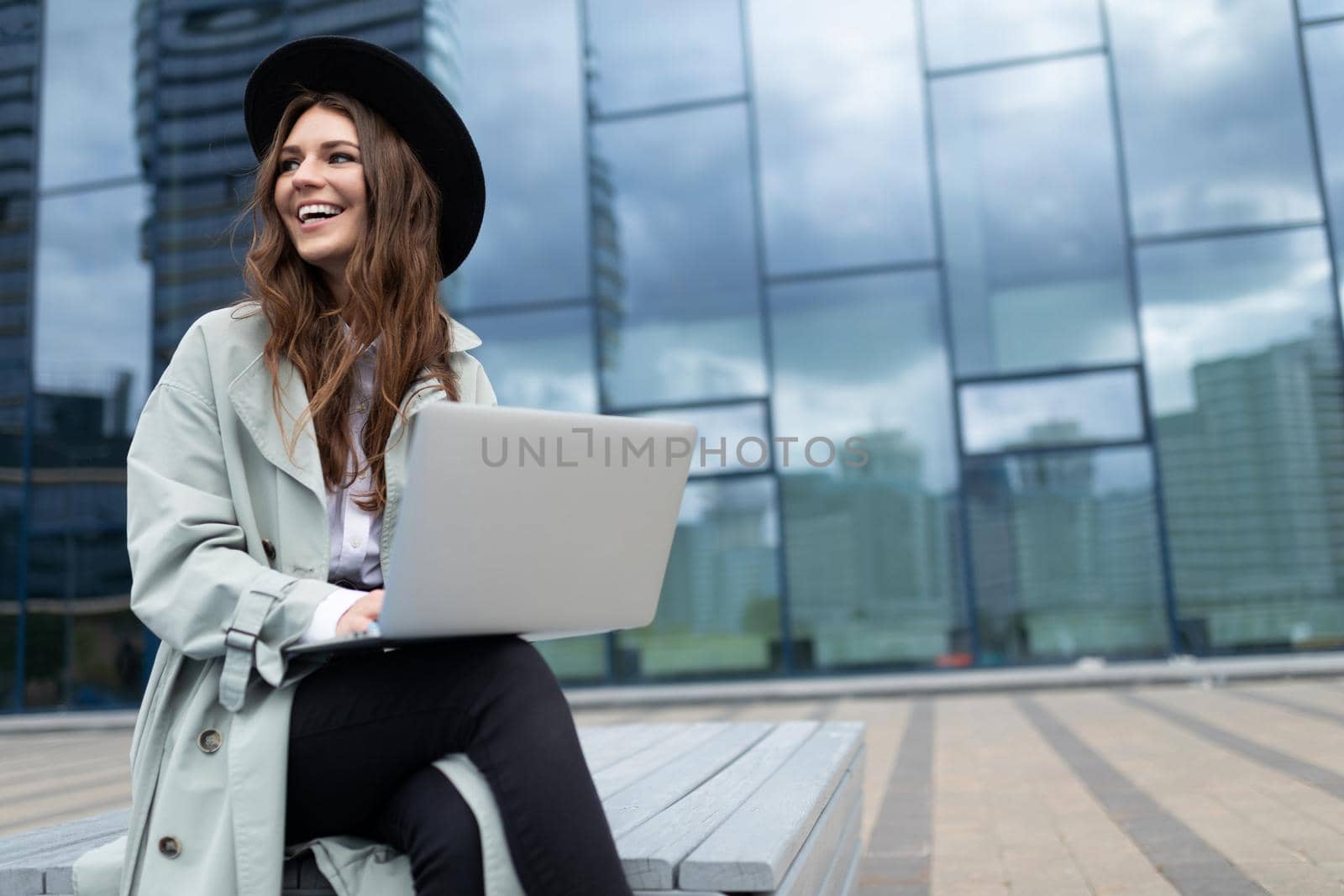 young stylish woman entrepreneur working on a laptop online against the background of the facade of an office modern building.