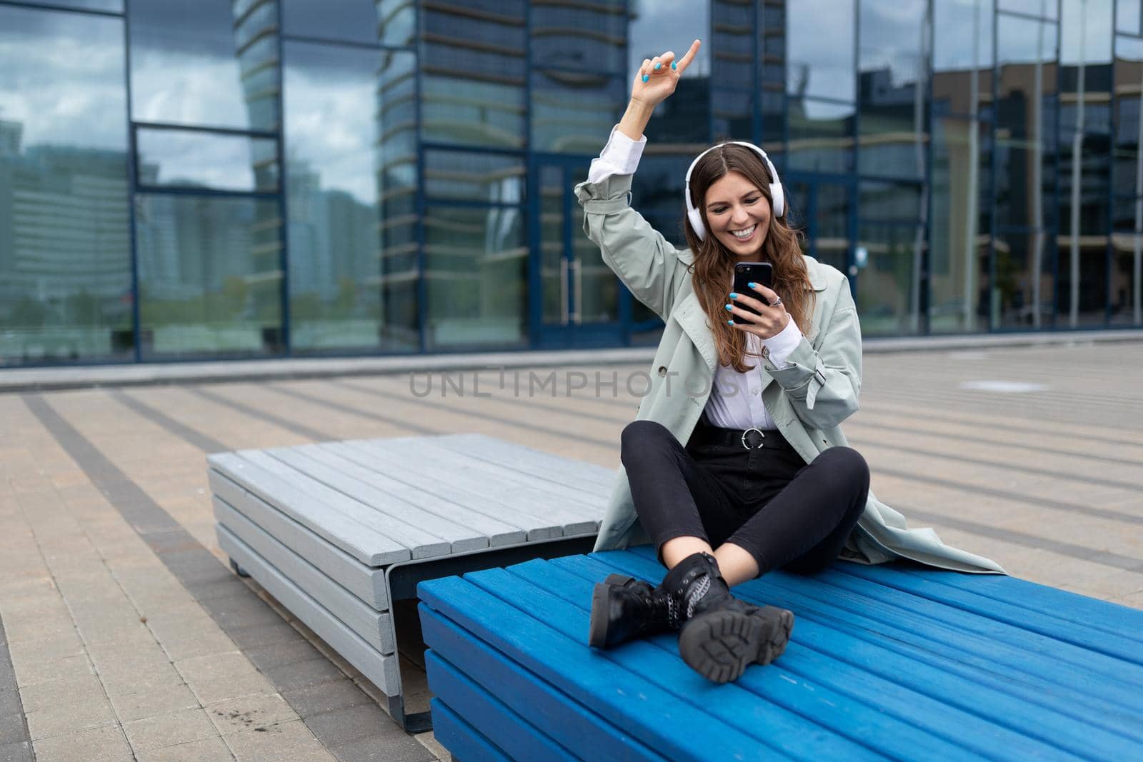young student listening to music Sitting on a bench in a yoga position dancing against the backdrop of a city building.