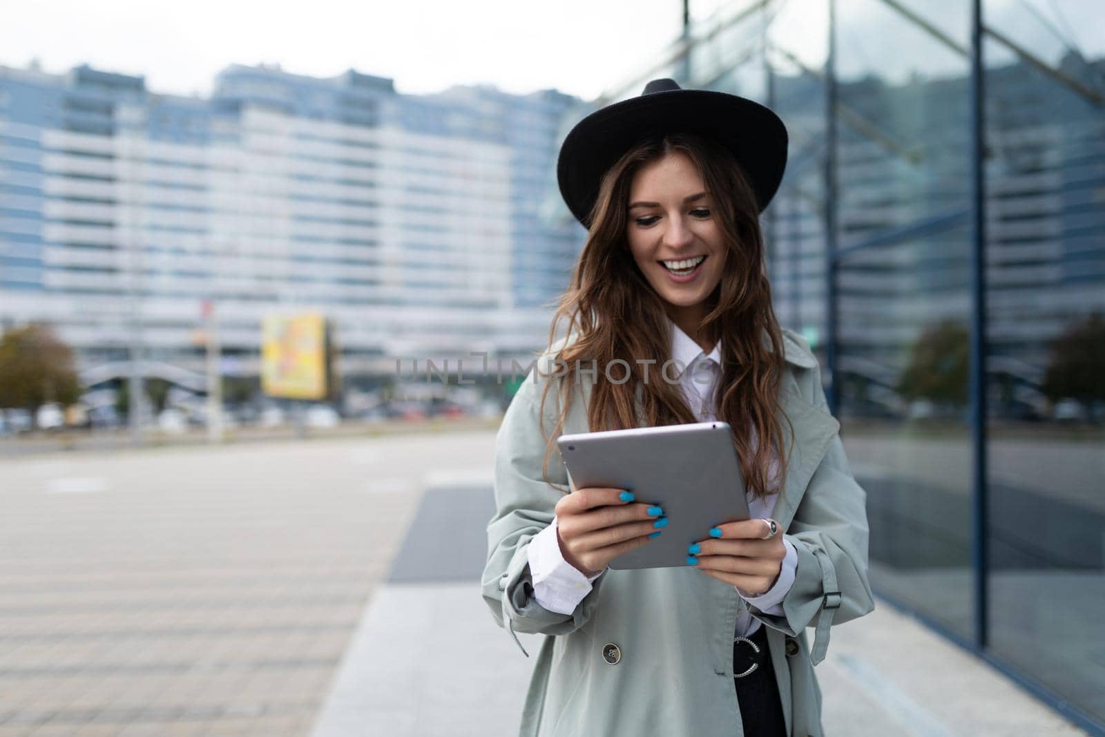 young stylish woman looking at a tablet against the backdrop of a glass facade of an office building in the city.