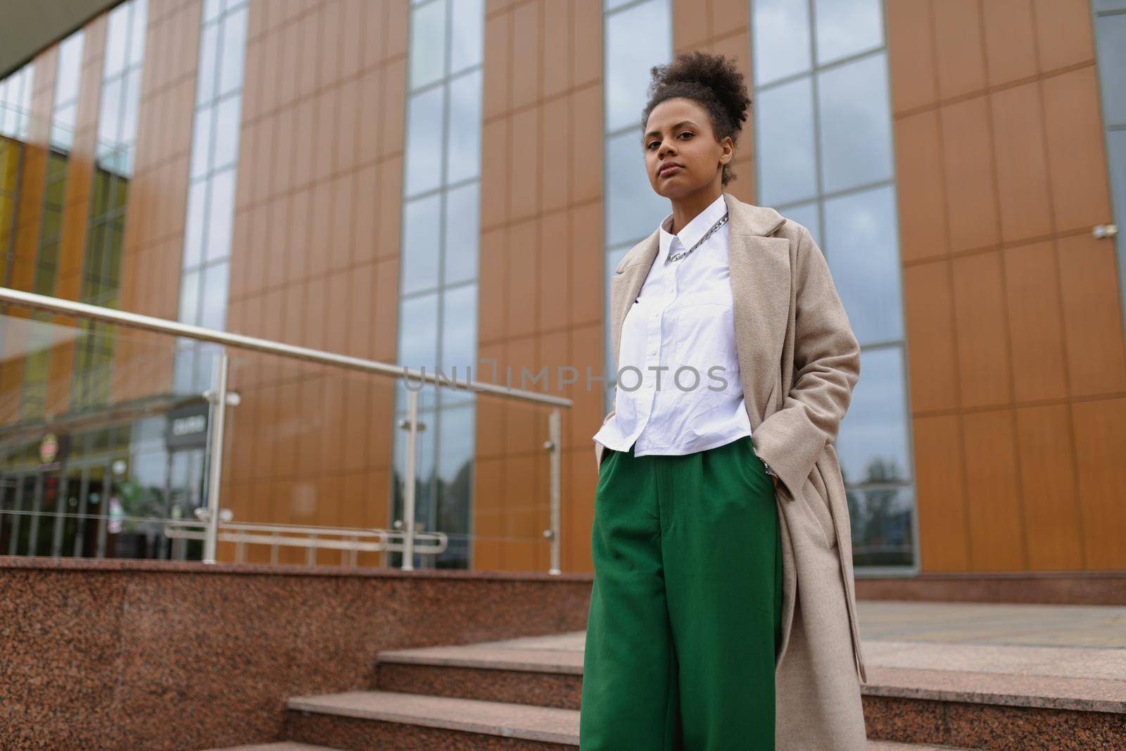 successful ambitious african american young woman with a serious face looks into the distance on the background of a city building.
