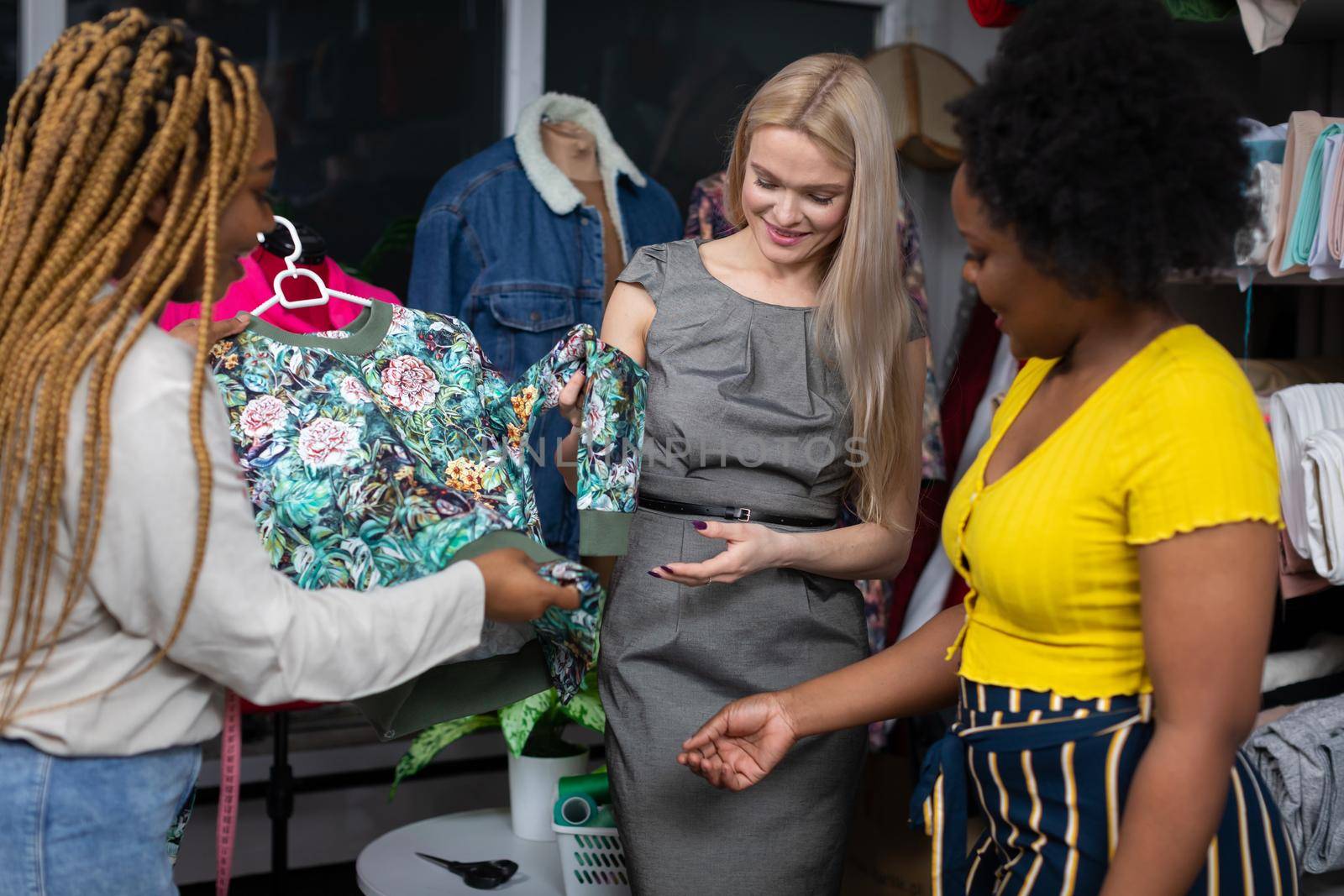 Dark-skinned sisters offer their new customer a blouse in shades of green with red amounts. Store and tailor store.