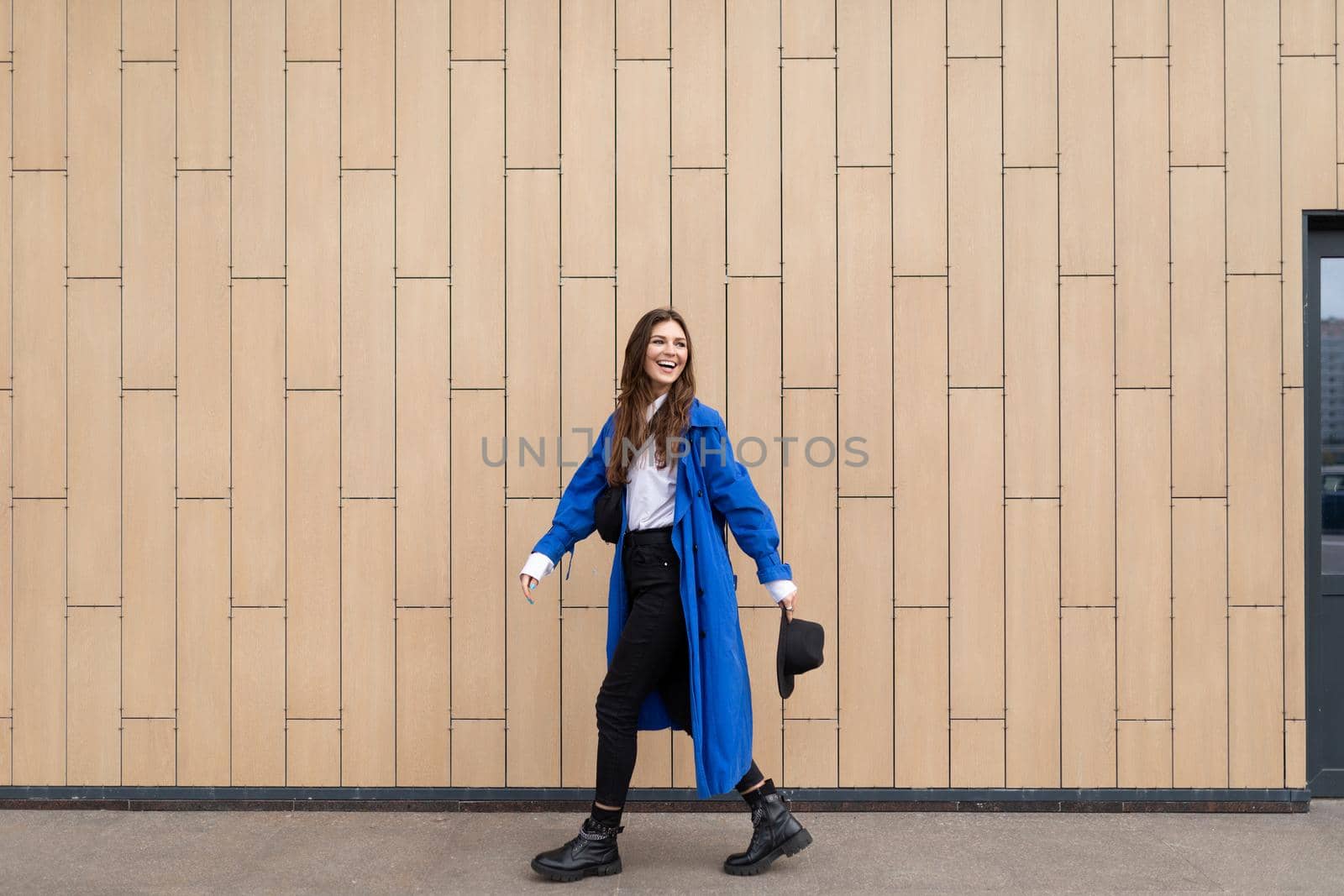 stylish woman in a blue autumn coat walks around the city against the background of a beige wall.