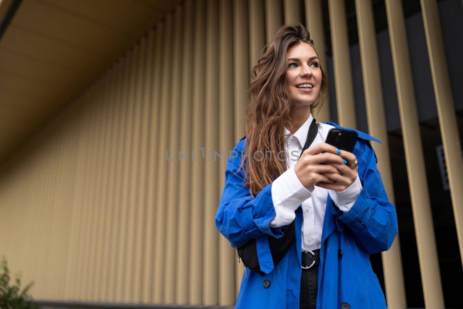 young female student with a mobile phone looking into the distance with a smile against the background of golden vertical stripes.
