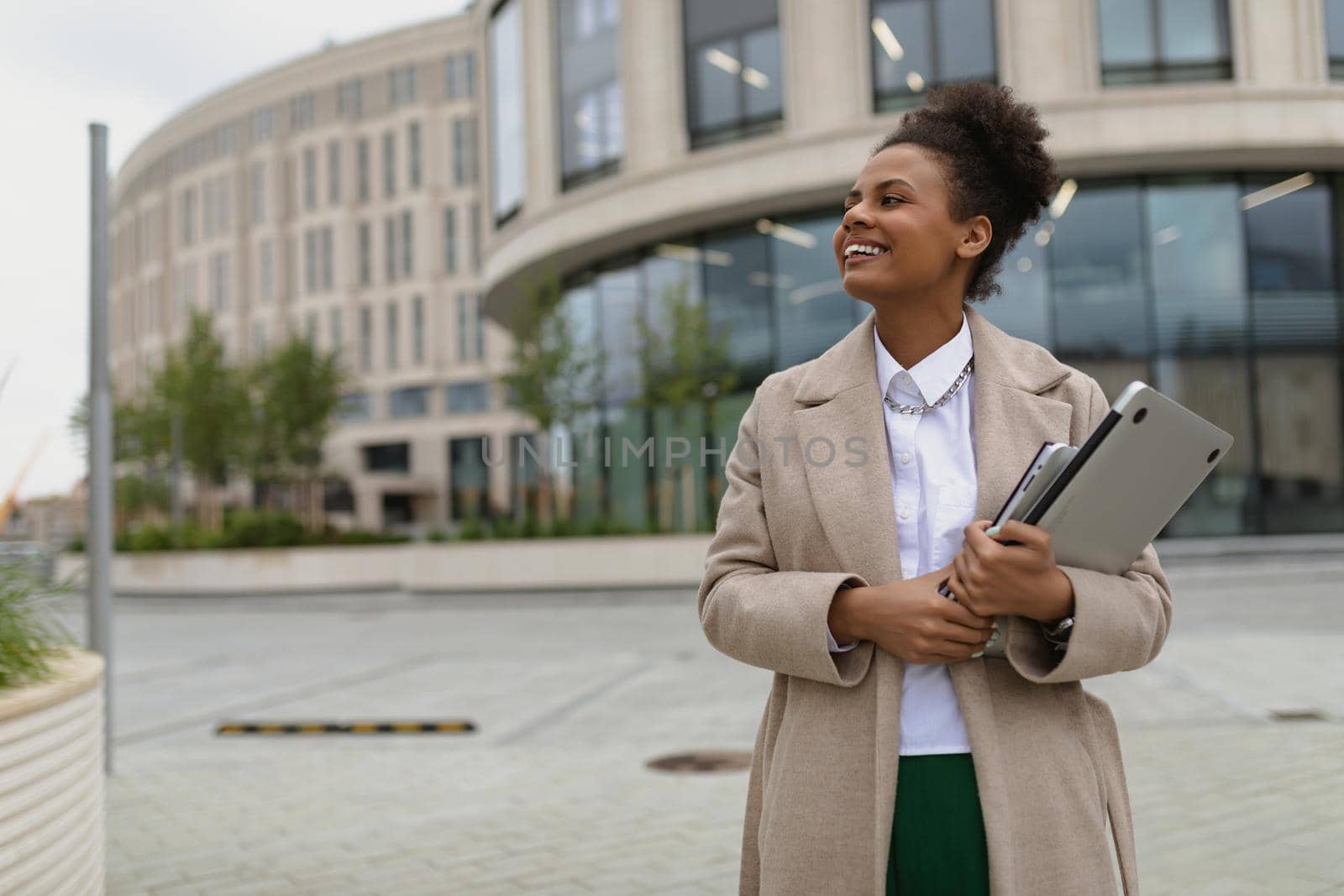 young satisfied african american woman walking around the city with a laptop and smiling.