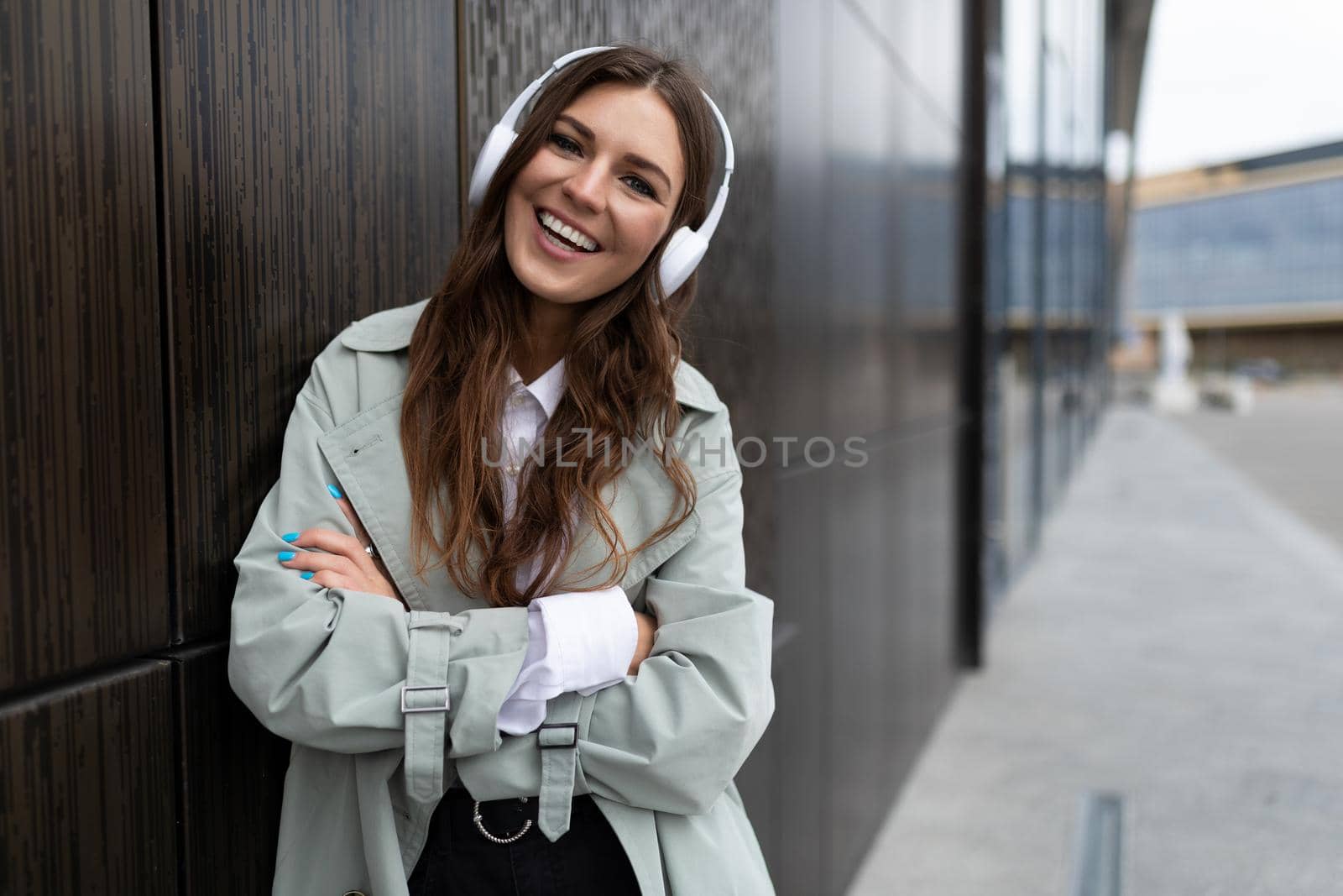young female student listening to music with headphones on the background of the city with a smile on her face.