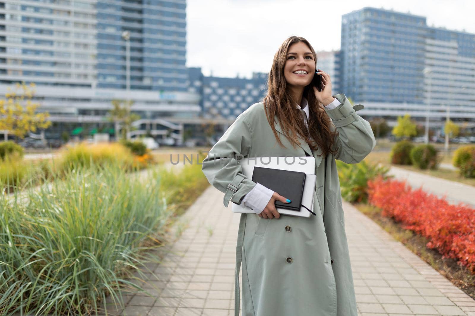 young woman student with a laptop weekly under her arm talking on the phone on the background of the city.