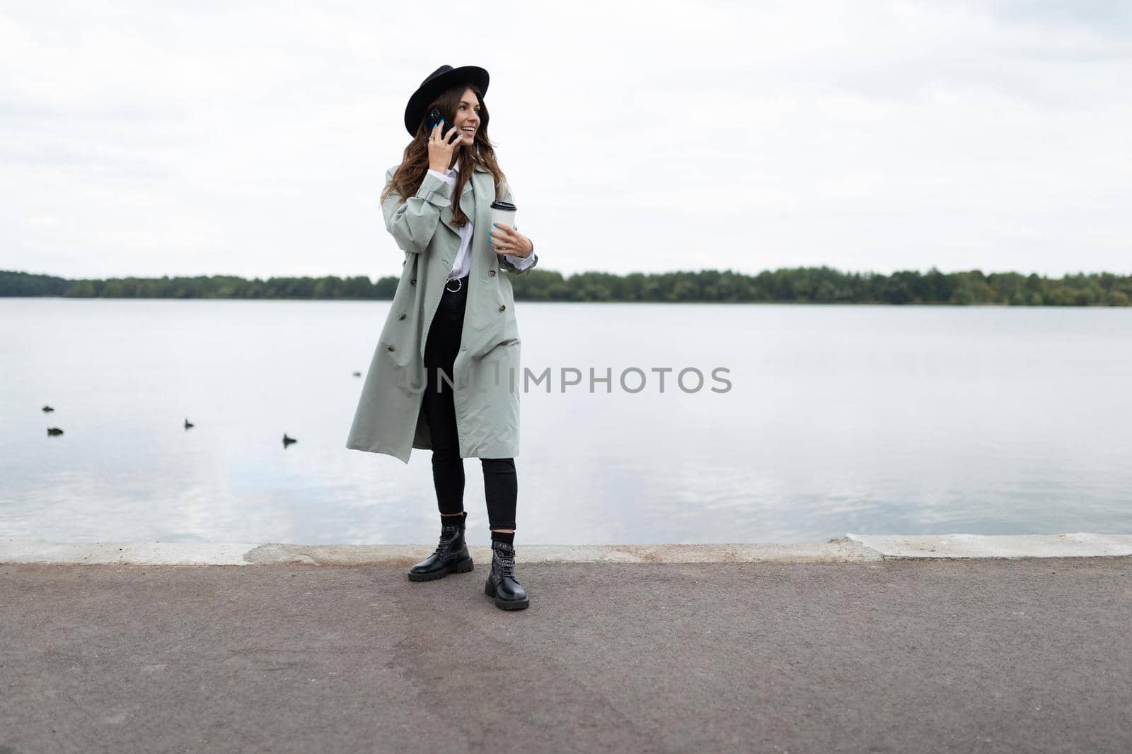 young stylish woman speaks on a mobile phone on the embankment against the background of the sea with a smile looks into the distance.
