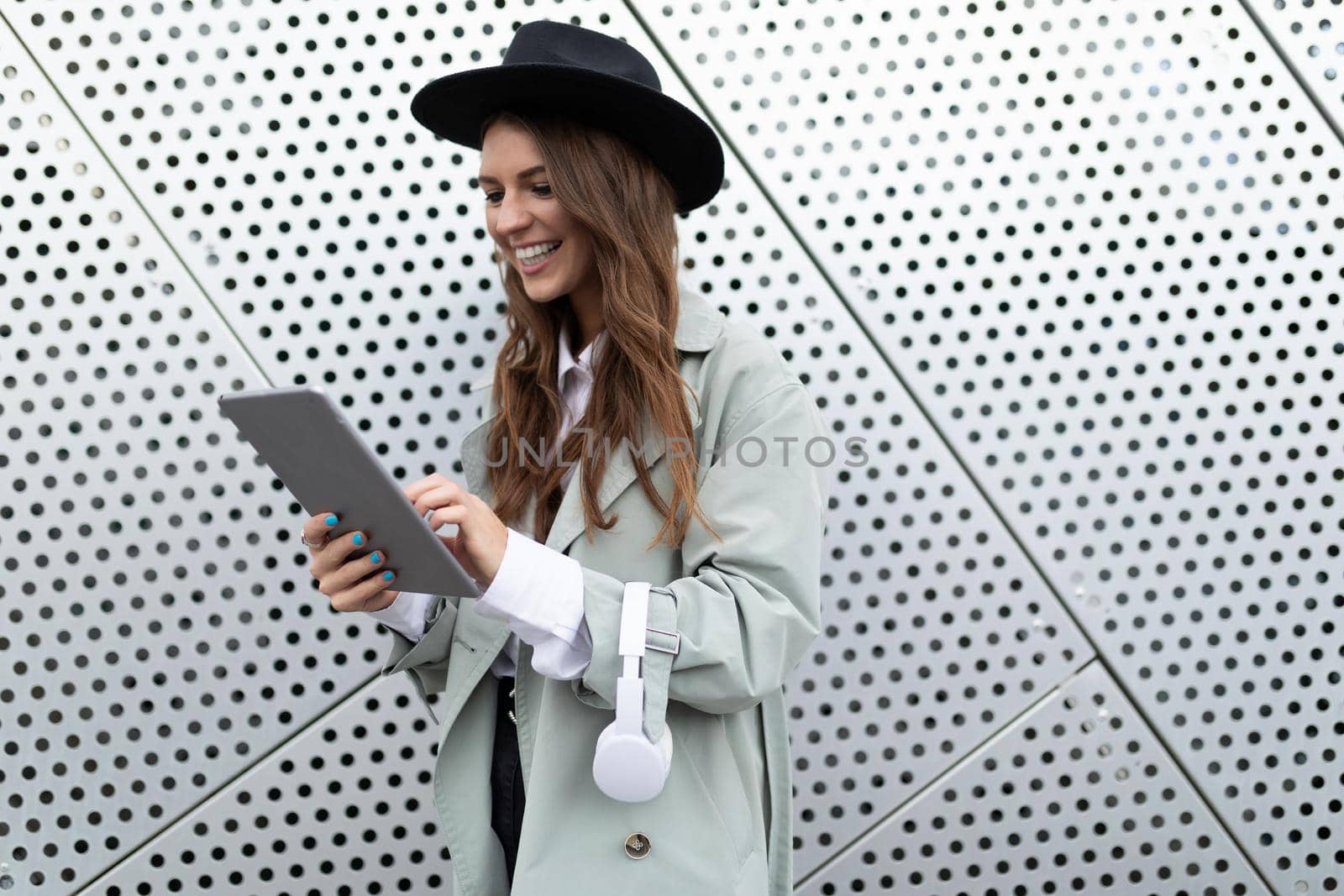 young cheerful woman in a black hat with headphones and a tablet smiling against the background of an aluminum facade Yes of an office building.
