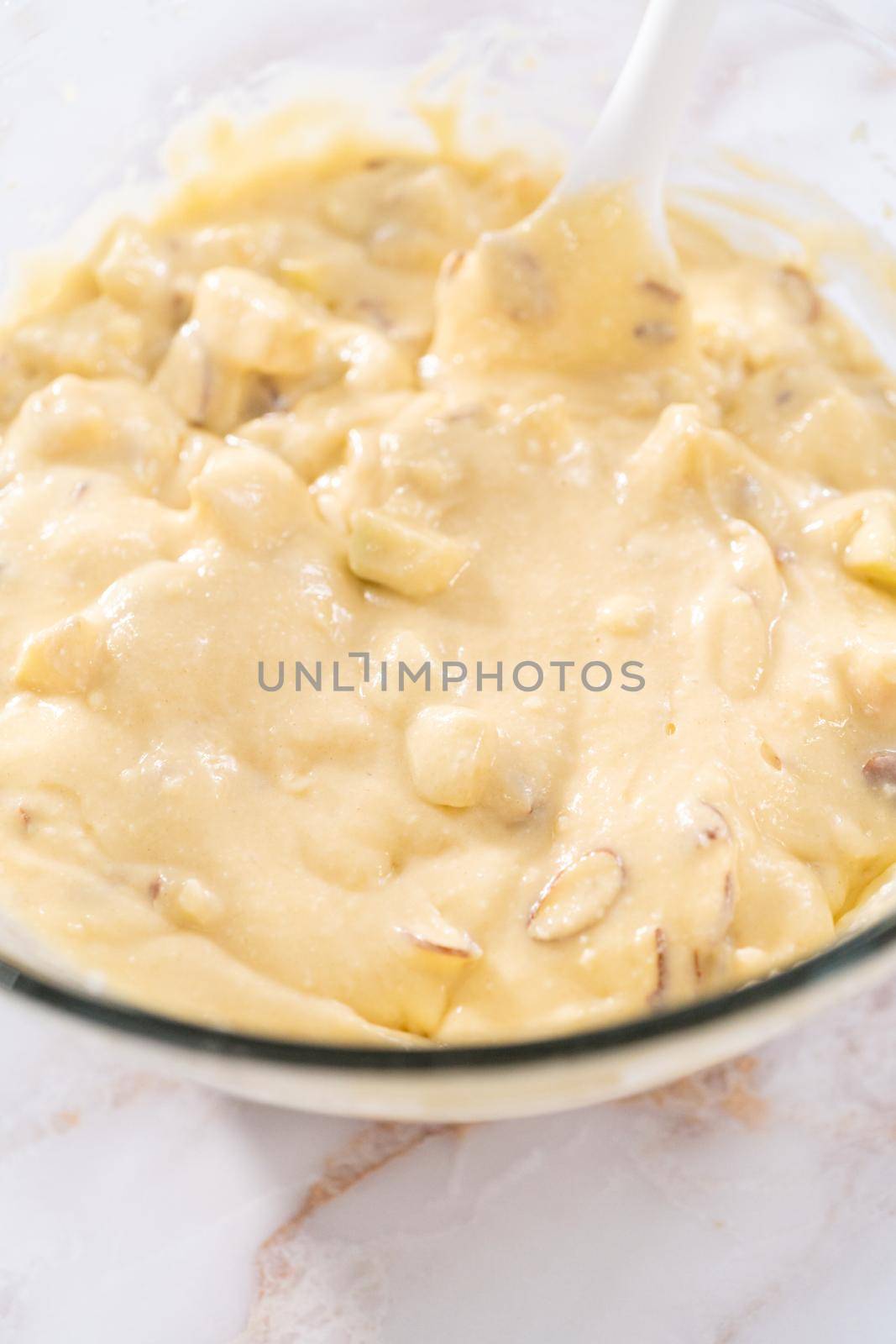 Mixing ingredients in a large glass mixing bowl to bake apple bundt cake with caramel glaze.