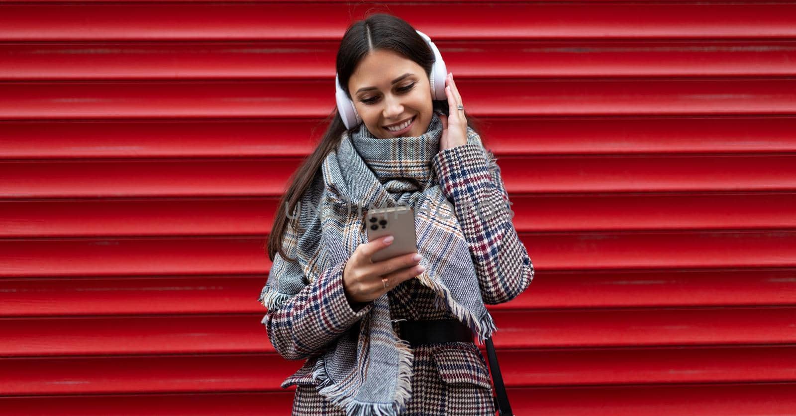 portrait of a young woman student in headphones with a mobile phone against the background of a red embossed wall.
