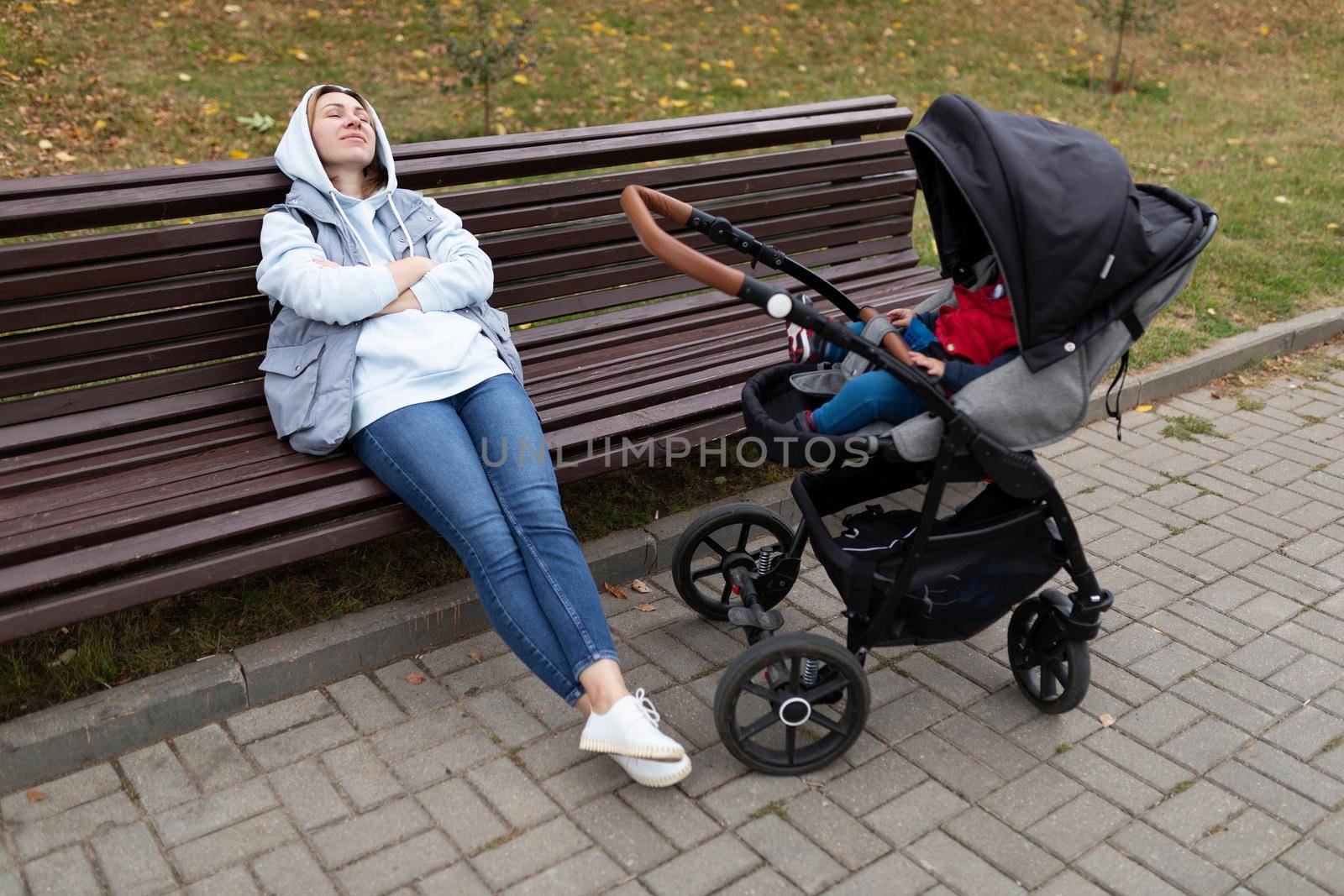 a young woman sleeps on a bench next to the stroller while walking with her small child.