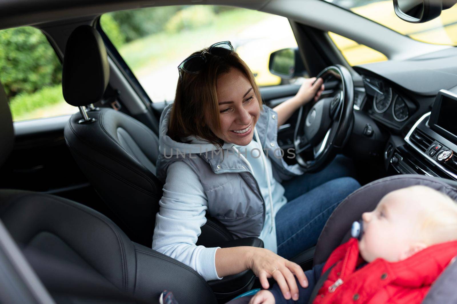 a young mother driving a car looks at a baby in a carrier in the front seat.