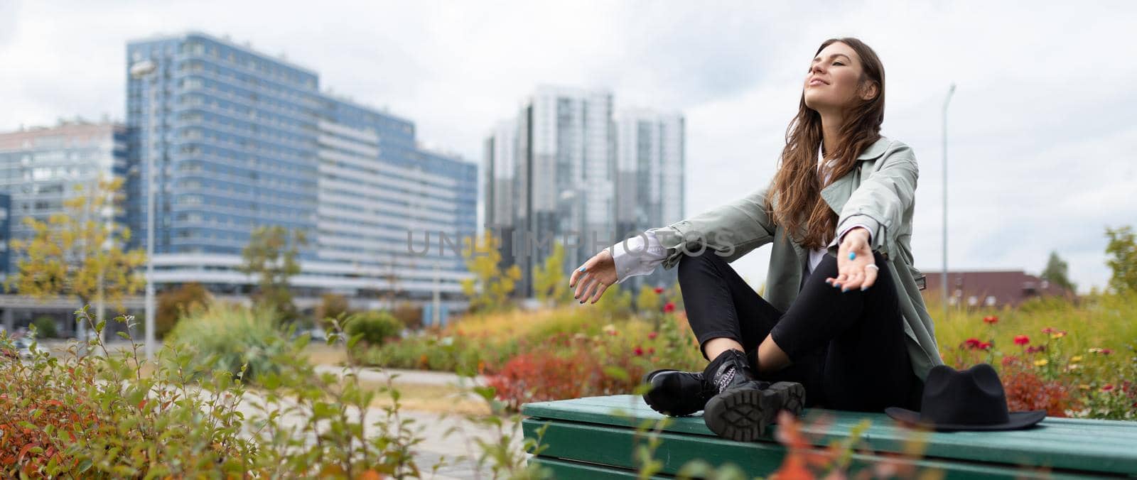 a young woman during a lunch break relax sitting in a yoga position in the park on the background of office buildings.