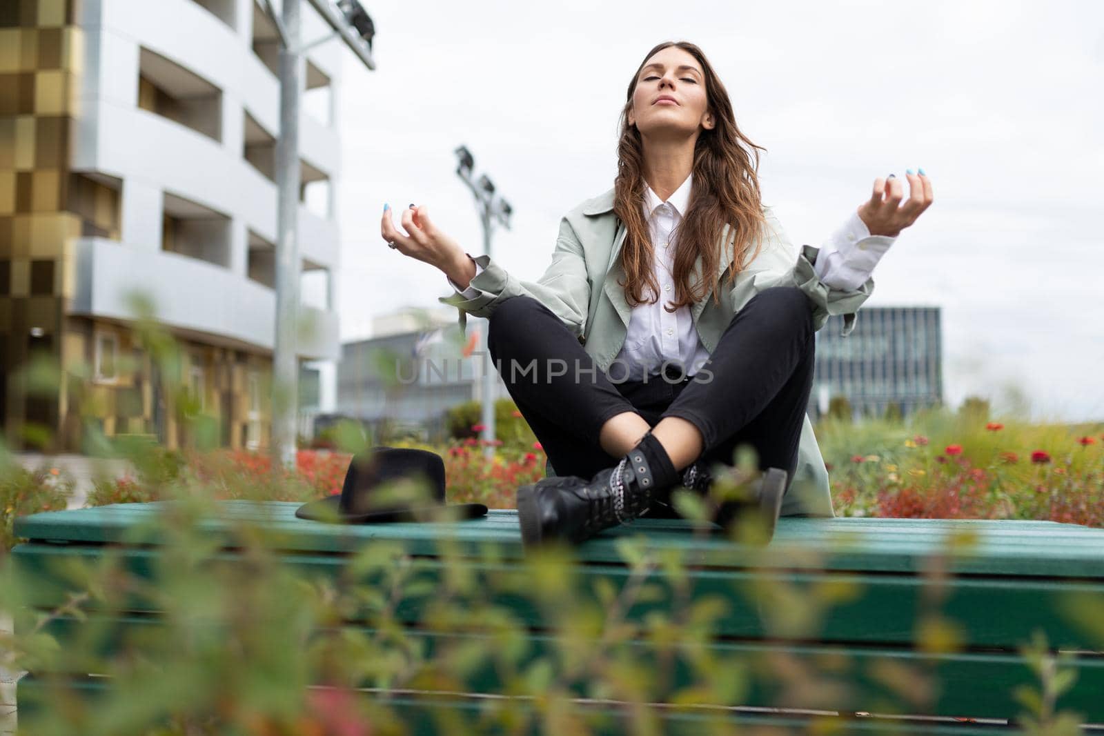 young stylish woman meditates during a lunch break in the park against the backdrop of an office building.