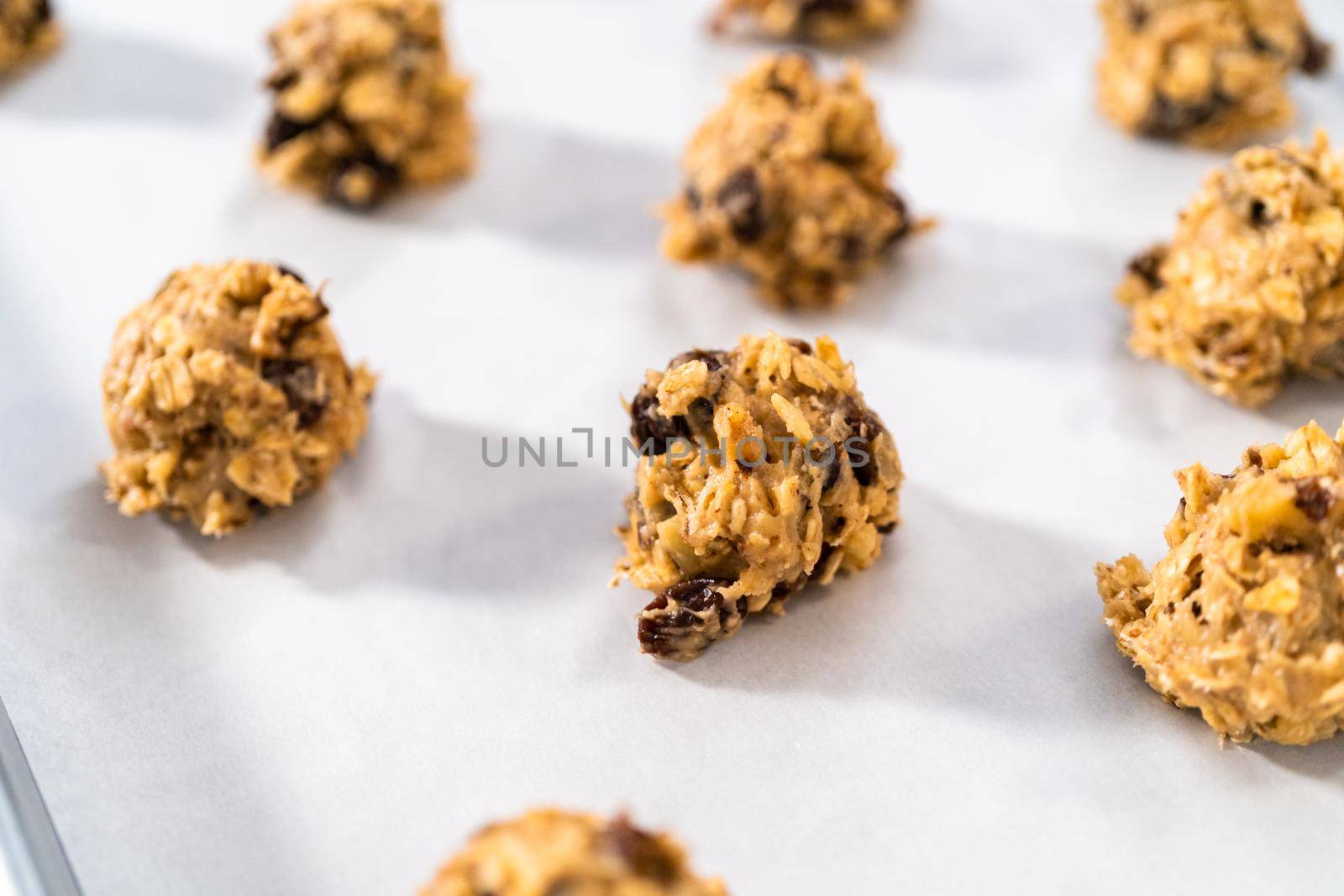 Scooping cookie dough with dough scoop into a baking sheet lined with parchment paper to bake soft oatmeal raisin walnut cookies.