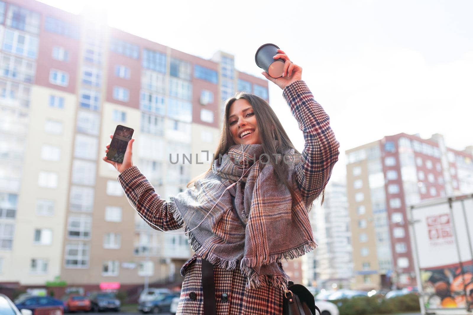 young successful satisfied with herself woman dancing listening to music in headphones from mobile phone on city panorama.