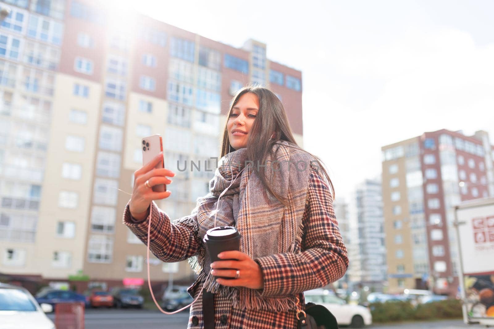 stylish young woman walking with a cup of coffee and taking a selfie in headphones.