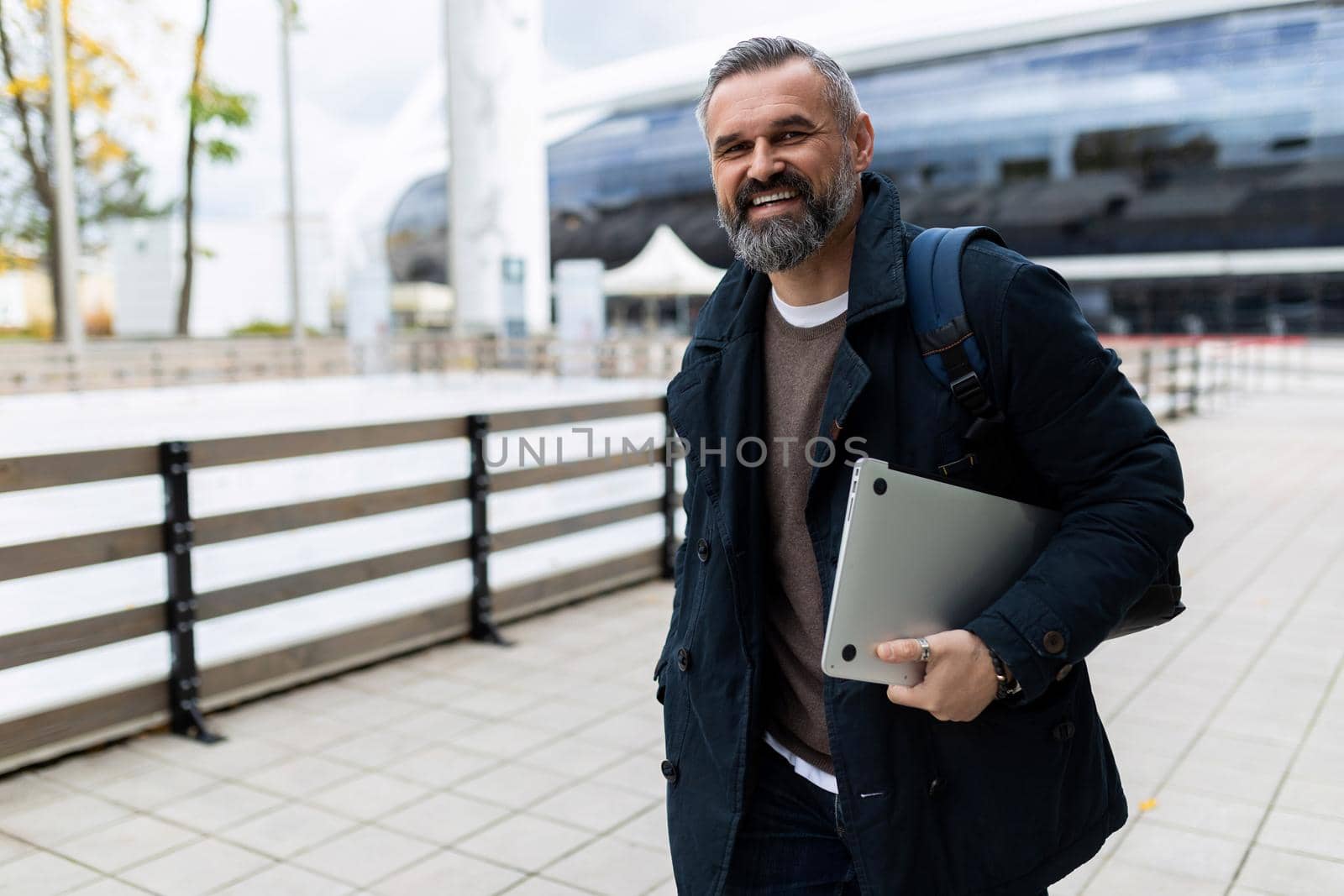 mature man with laptop and backpack hurrying to work smiling looking at camera.