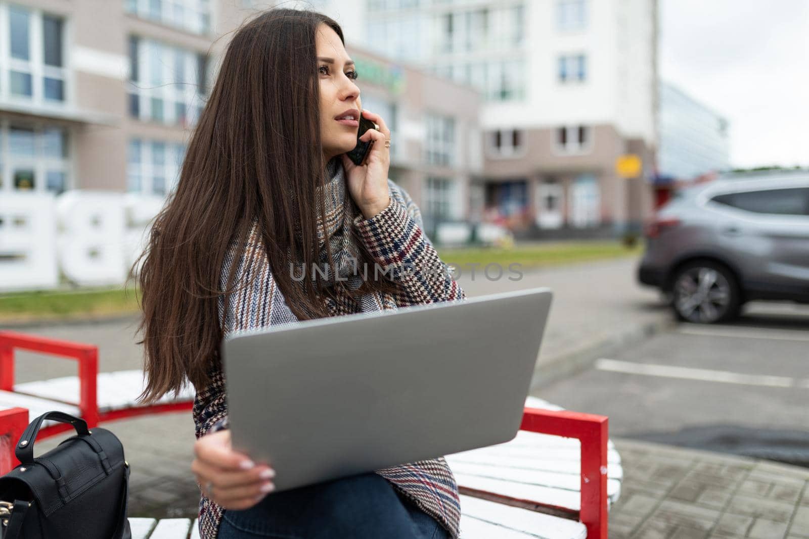 a young woman on the way to the office works on a laptop and makes a phone call on the background of the city.