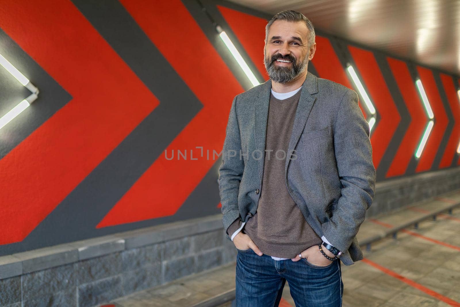 portrait of a mature bearded businessman with a smile in a gray stylish jacket against a wall with red arrows.