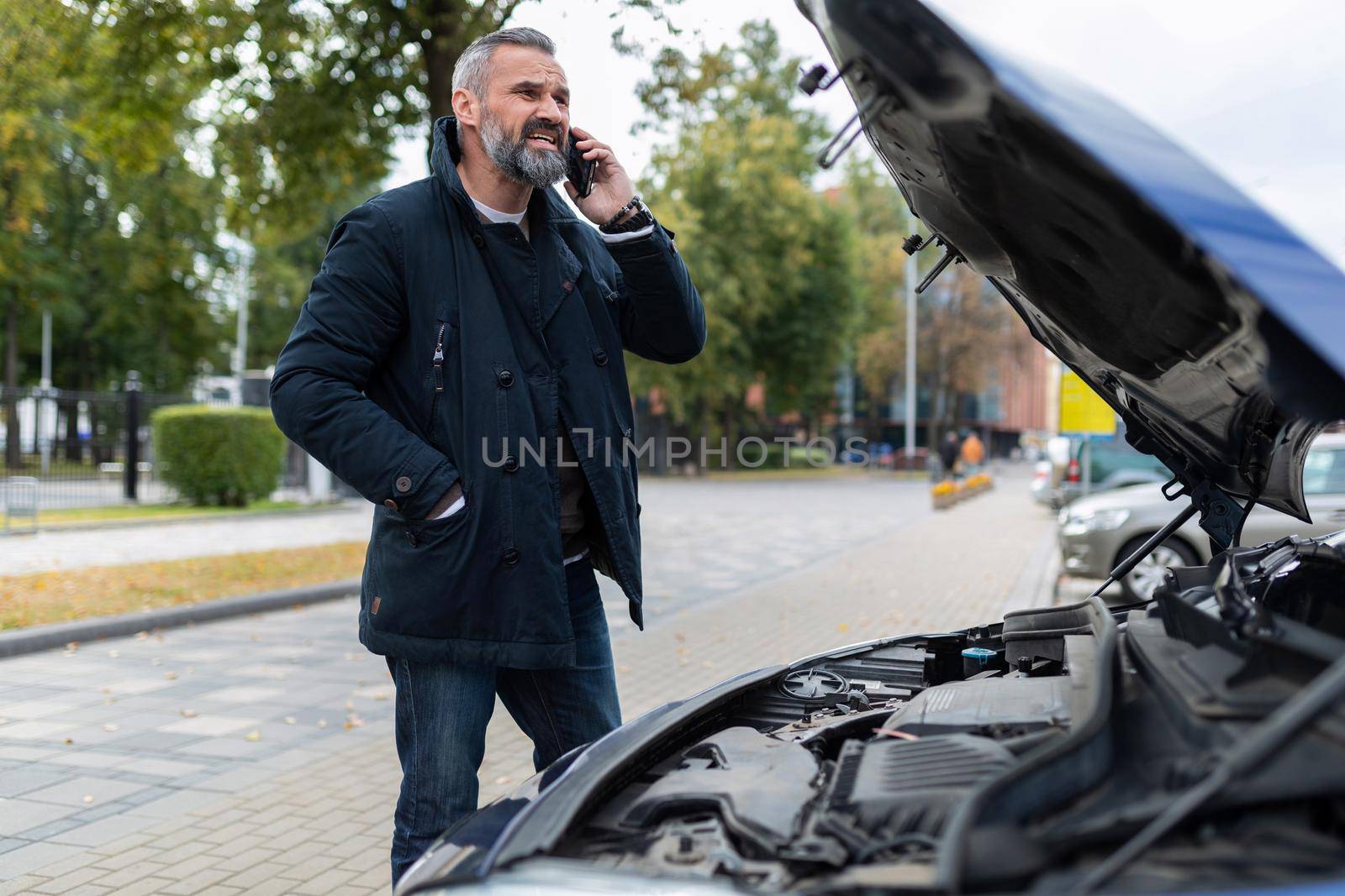 a man calls a tow truck next to a broken car in the city.
