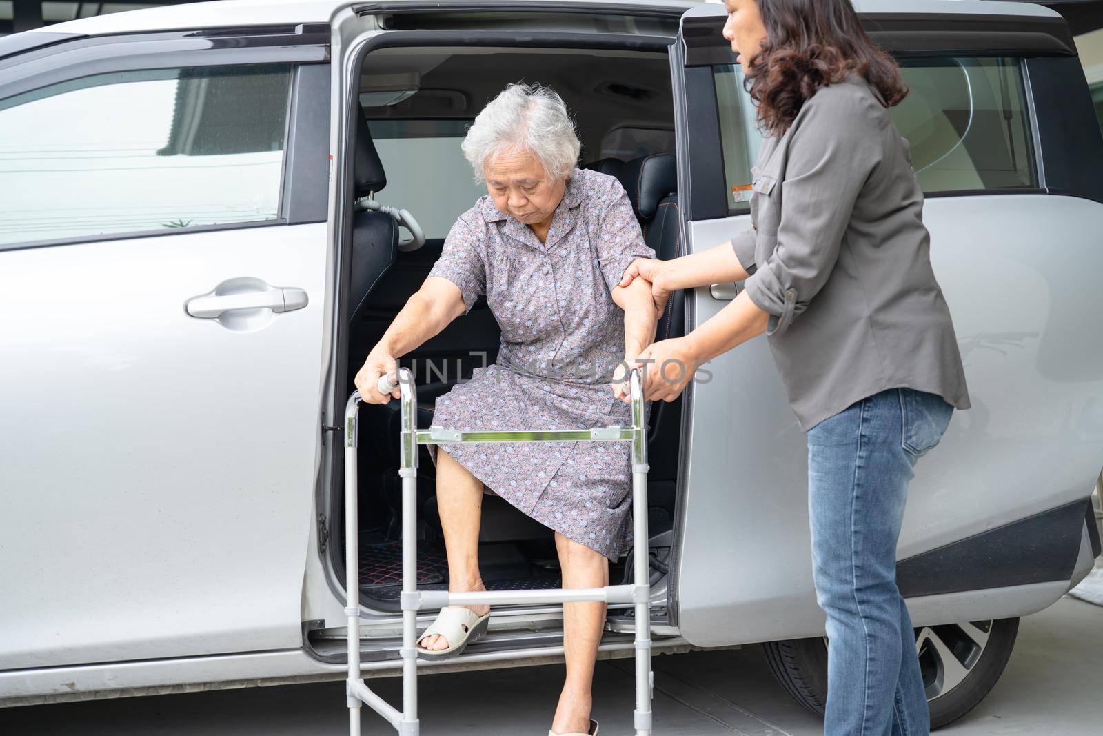 Caregiver daughter help and support asian senior or elderly old lady woman patient prepare get out her car.