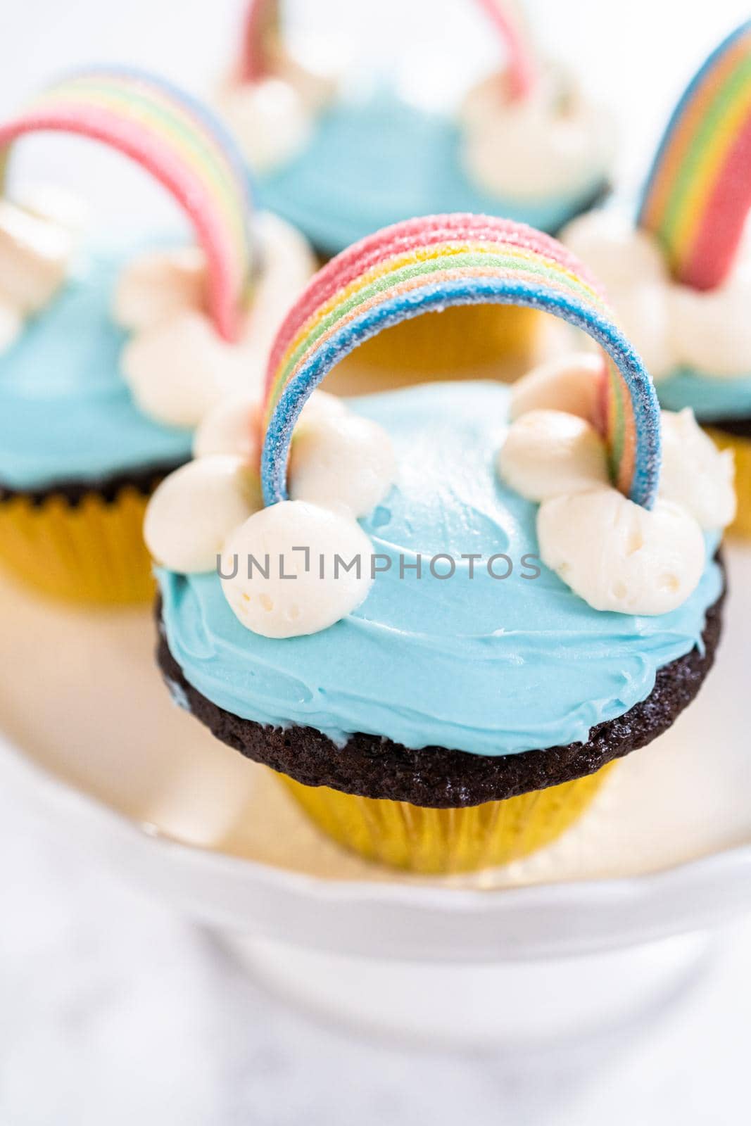 Chocolate cupcakes decorated with blue buttercream frosting and rainbow for unicorn theme birthday party.