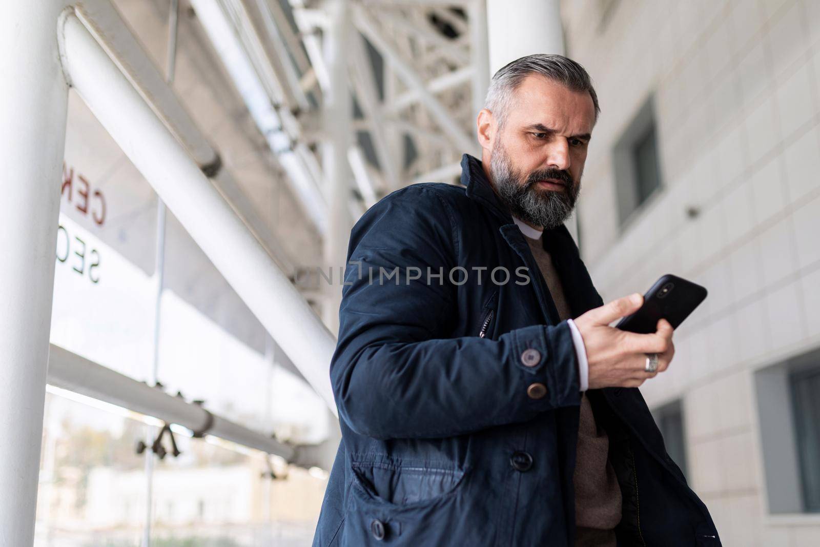 mature man waiting for boarding a flight at the airport looking at his mobile phone.