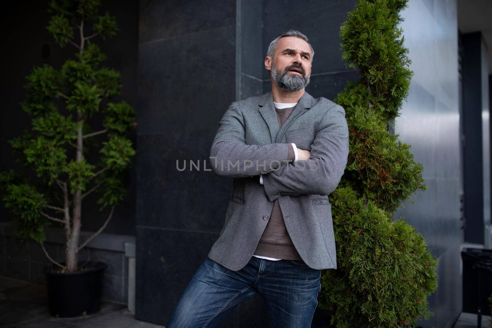 a serious elderly businessman in a gray jacket next to the entrance to the office building looks into the distance in thought.