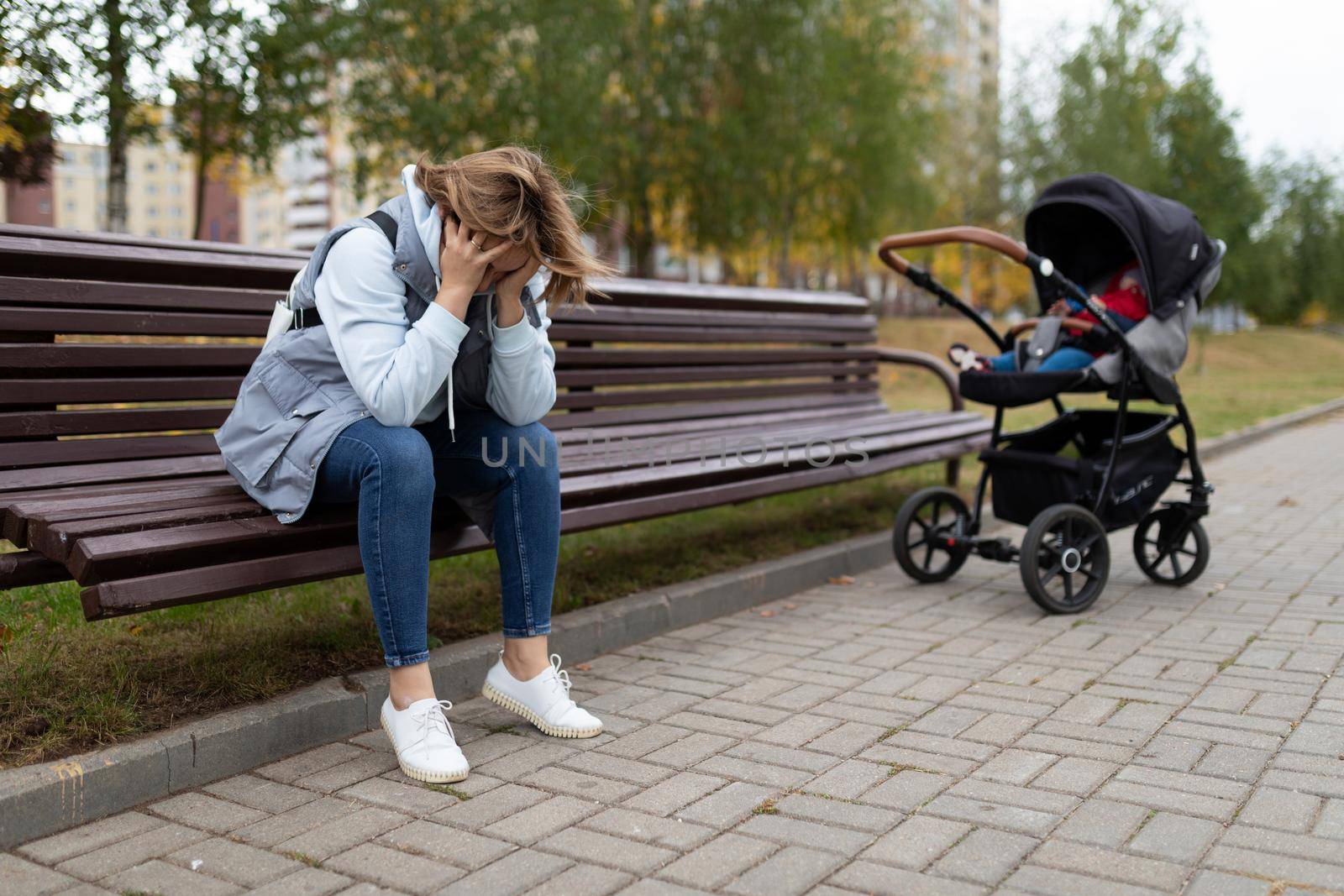 a young mother sits on a bench upset next to a baby stroller, Concept of postpartum depression.