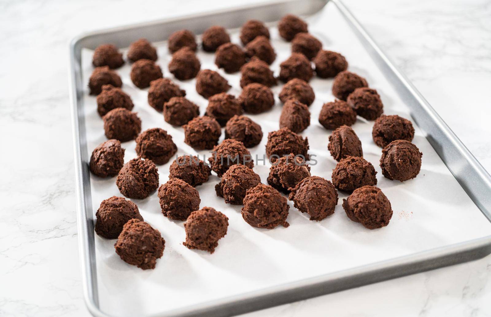 Scooping cookie dough with a small dough scoop into a baking sheet lined with parchment paper to bake peppermint white chocolate cookies.