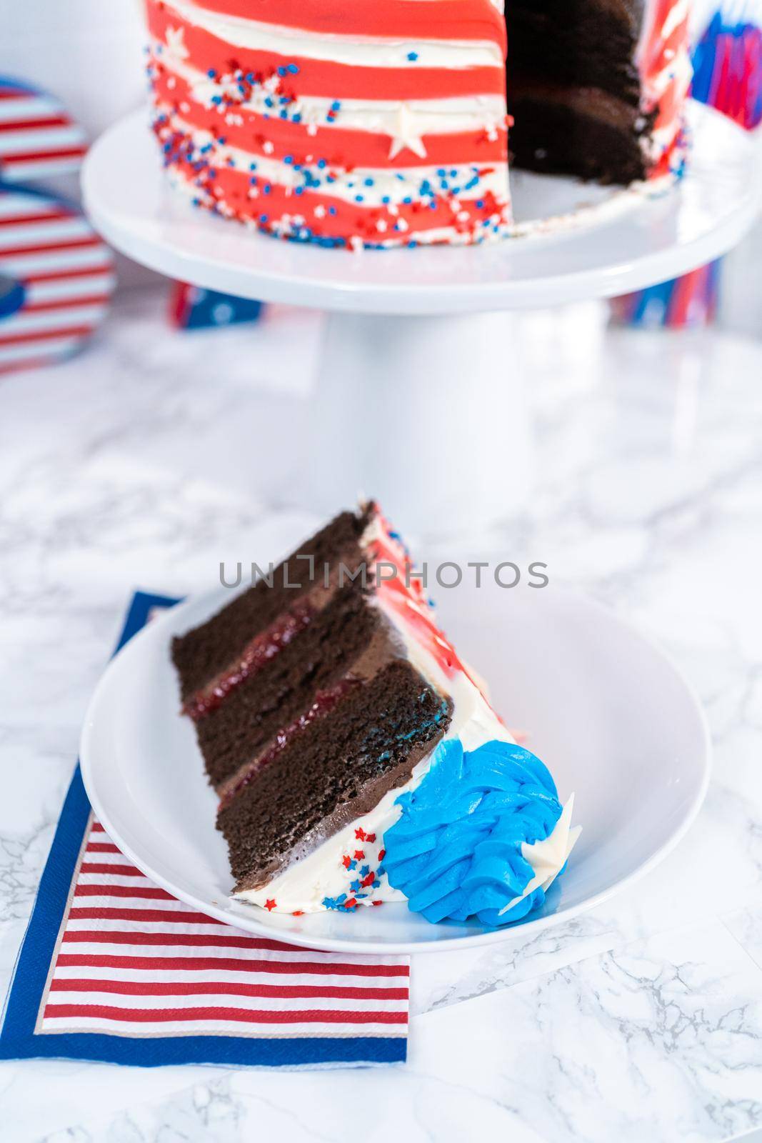 Slice of July 4th chocolate cake decorated with red, white, and blue buttercream frosting on a white plate.