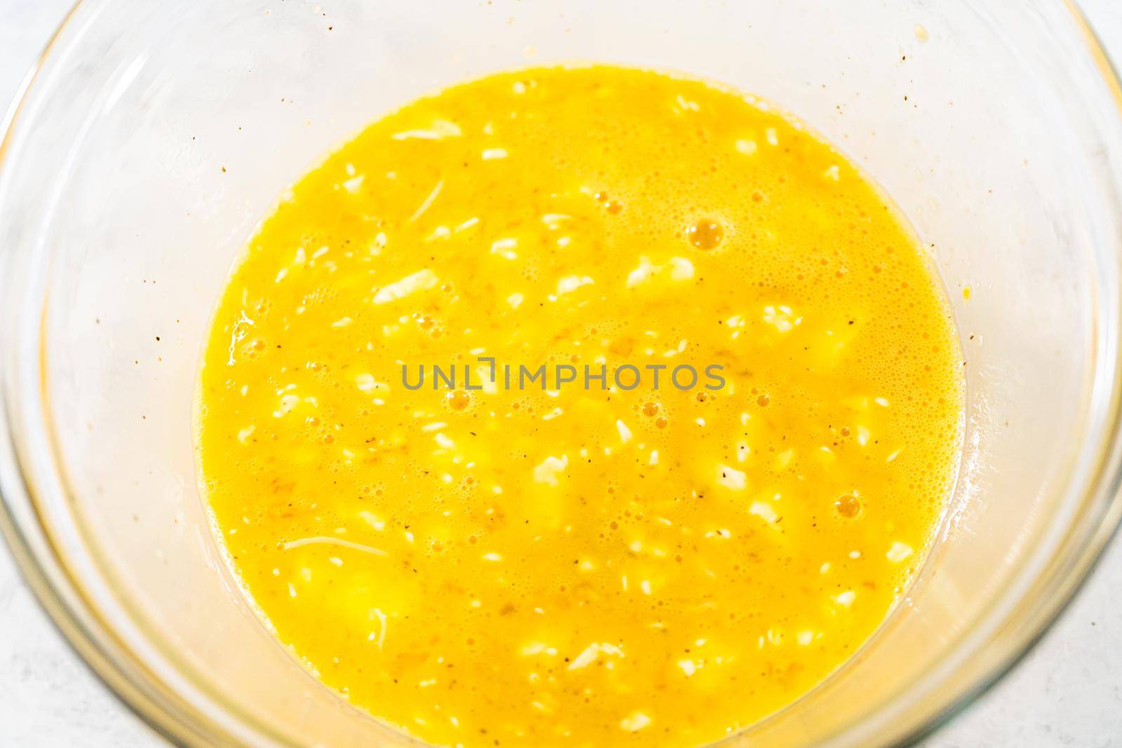 Mixing ingredients with a hand whisk in a glass mixing bowl to make egg bites.