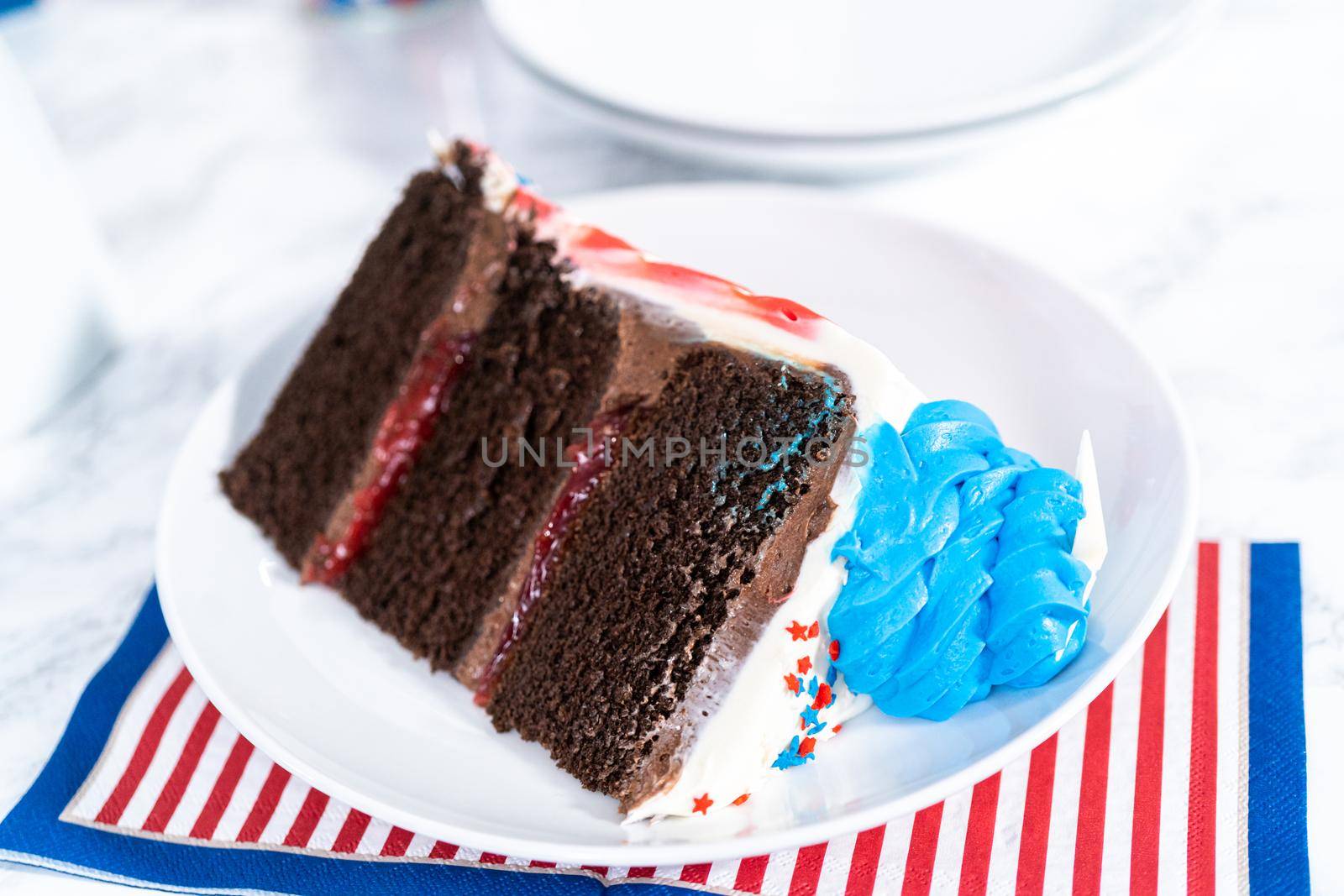 Slice of July 4th chocolate cake decorated with red, white, and blue buttercream frosting on a white plate.