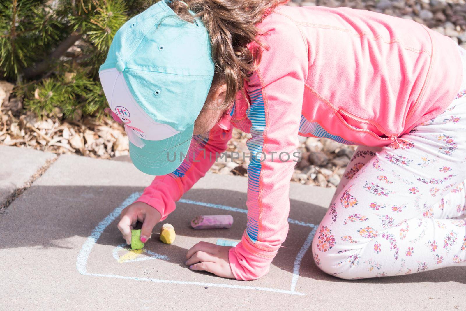 Little girl playing with chalk on a driveway in front of the house.