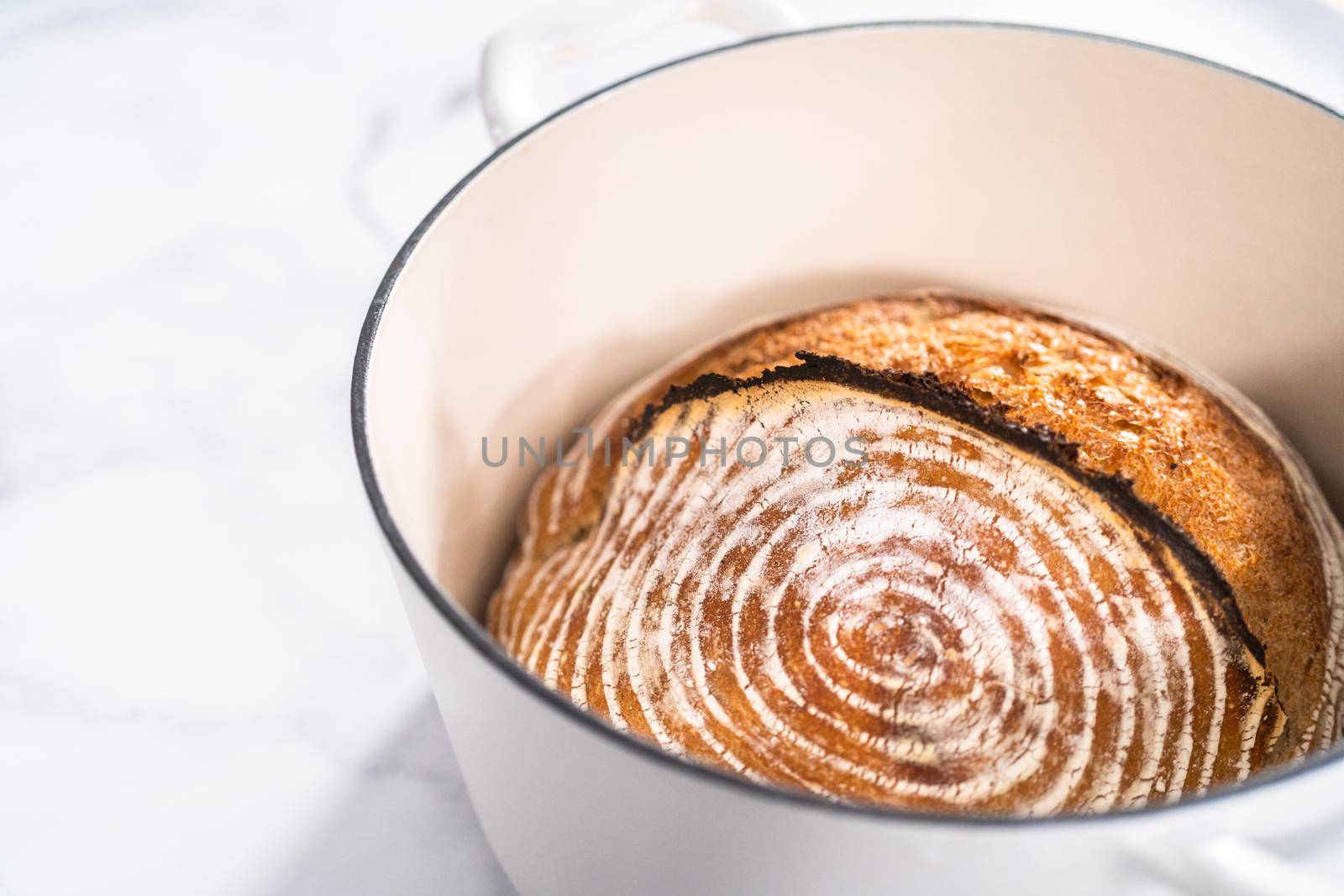 Freshly baked loaf of a wheat sourdough bread with marks from bread proofing basket in enameled cast iron dutch oven.